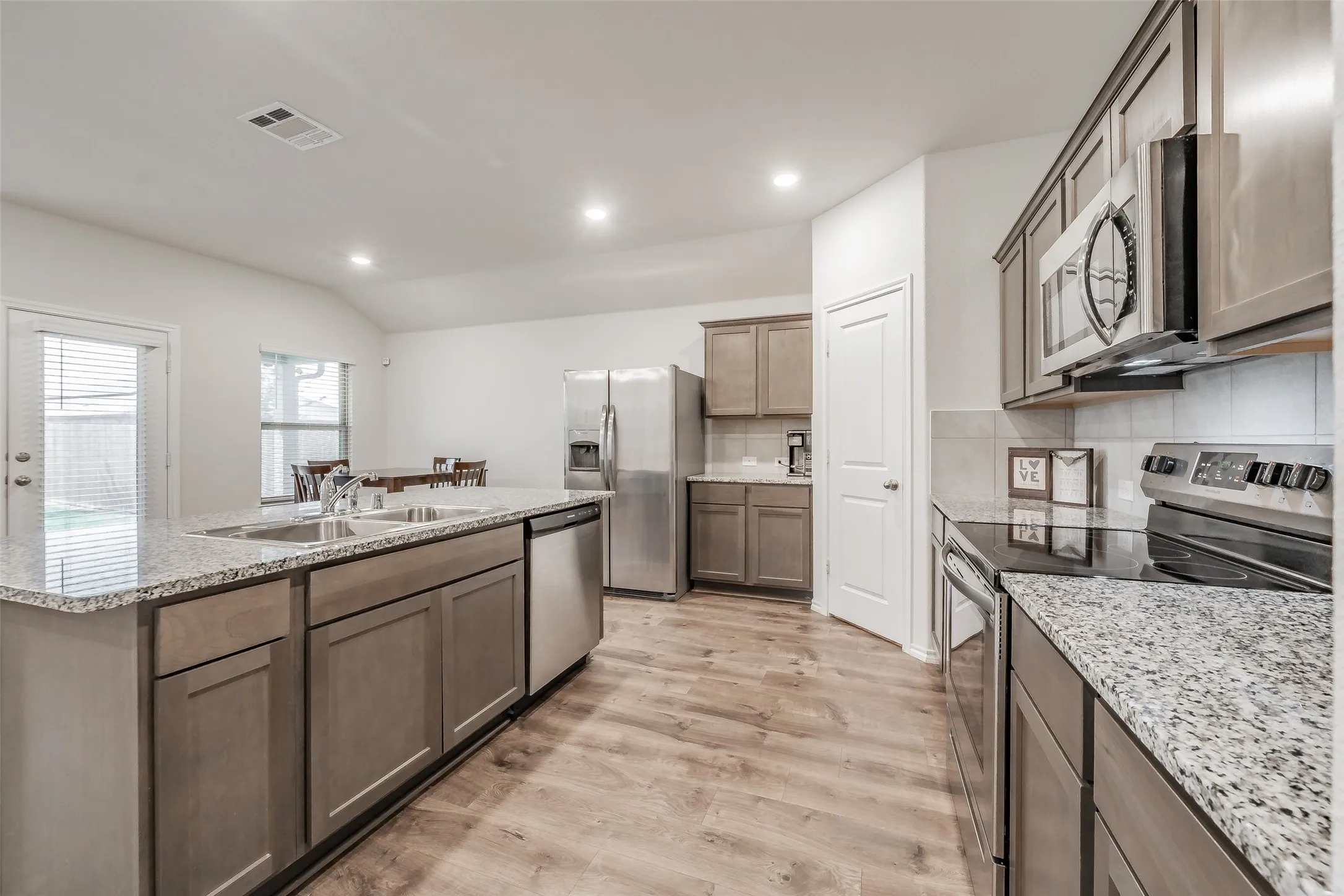 Kitchen featuring wood-finish flooring, recessed lighting, stainless steel appliances, a kitchen island with a double basin sink, and ample cabinetry
