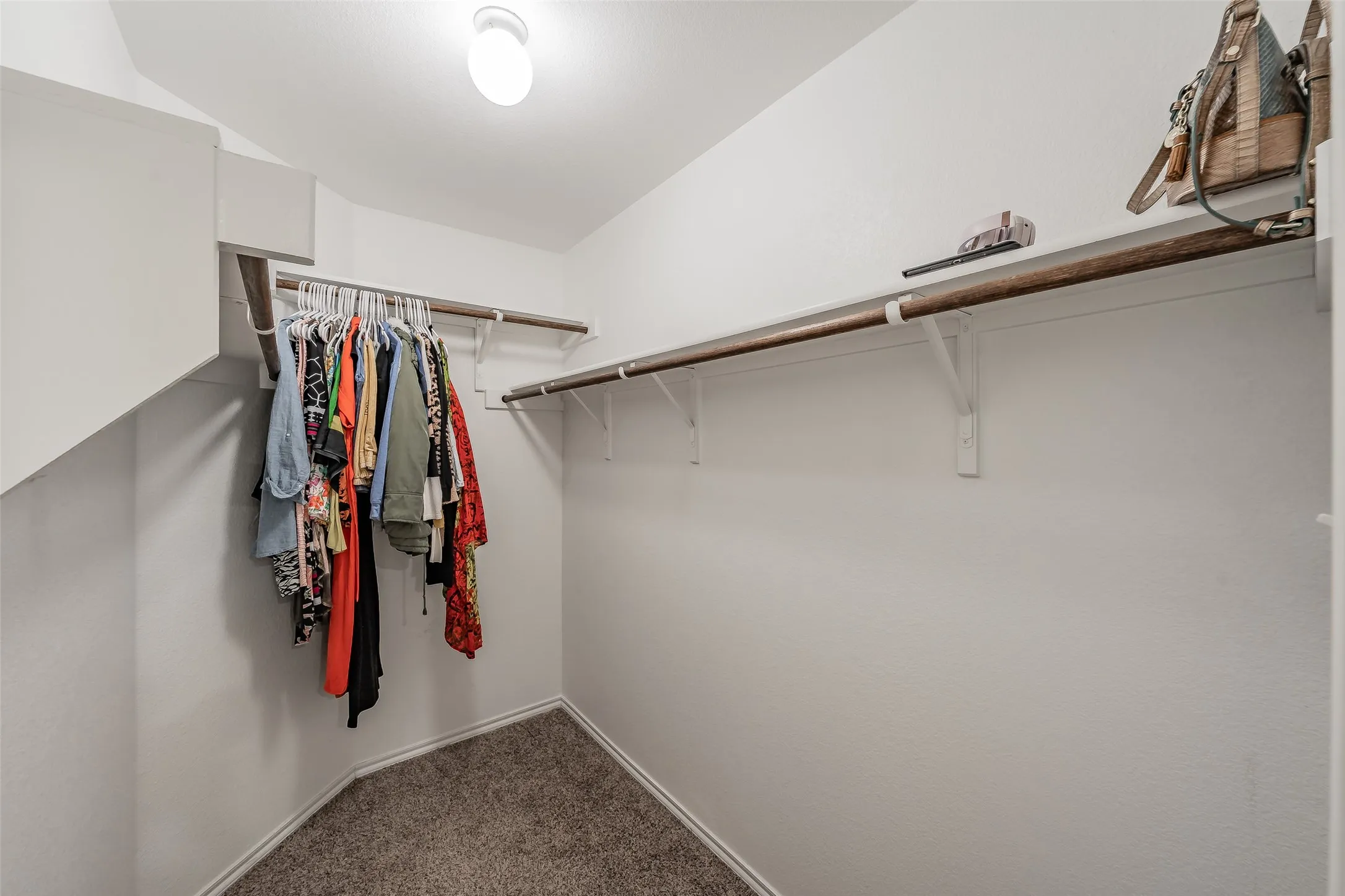 Carpeted primary walk-in closet with white walls, two permanent shelving units, and overhead lighting