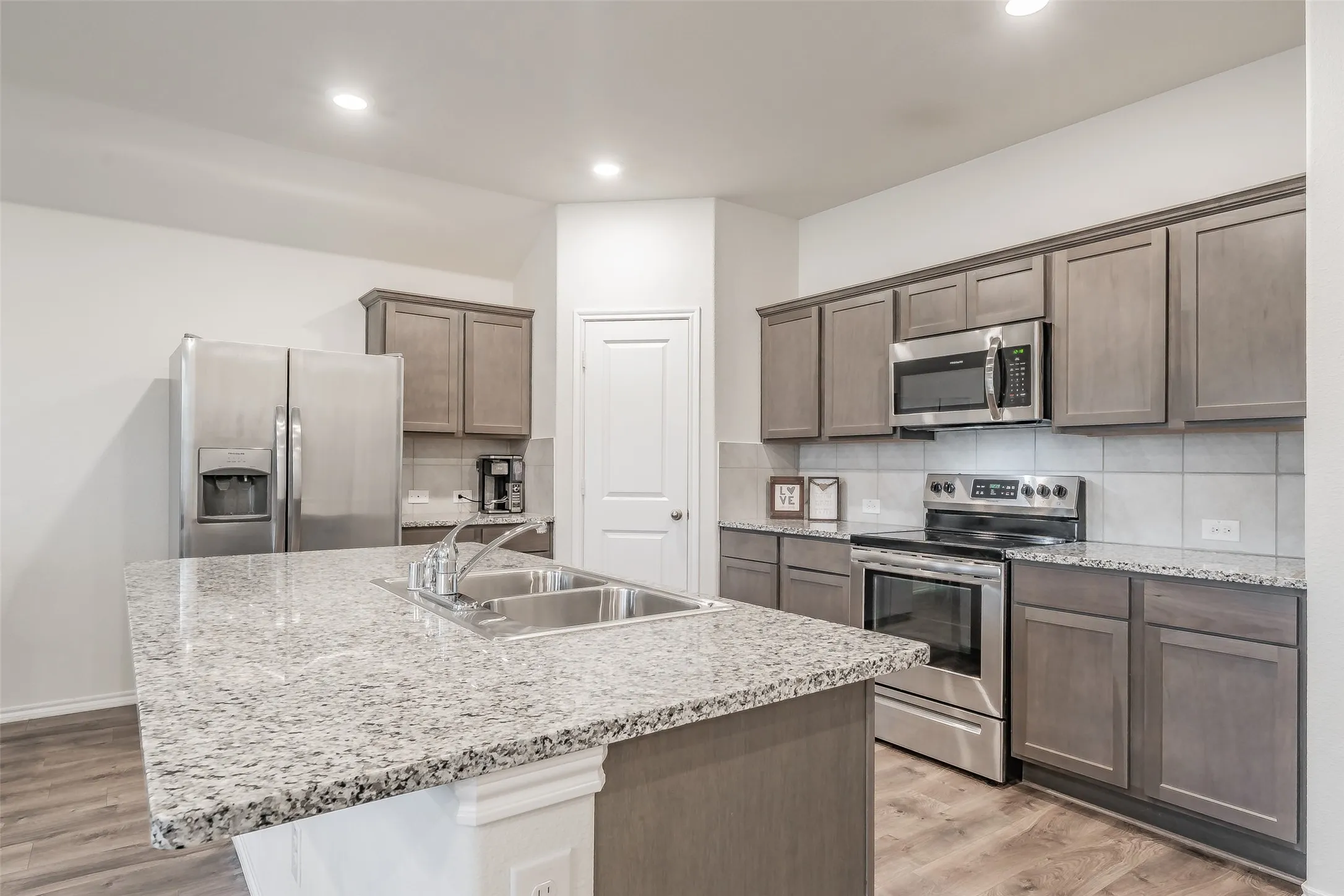 Kitchen featuring a large central island with a double basin sink, granite-style countertops, stainless steel appliances, and wood-finish flooring