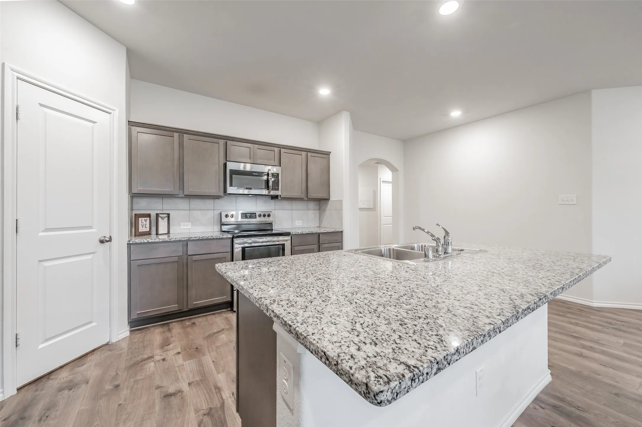 Kitchen featuring an island with a dual basin sink, stainless steel appliances, grey cabinetry, and wood-finish flooring