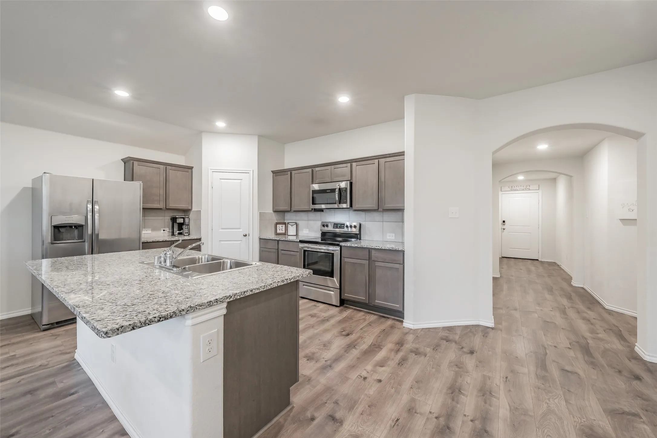 Kitchen featuring an island with a dual-basin sink and stone-finish countertop, wood-finish flooring, recessed lighting, and stainless steel​​‌​​​​‌​​‌‌​‌‌​​​‌‌​‌​‌​‌​​​‌​​ appliances