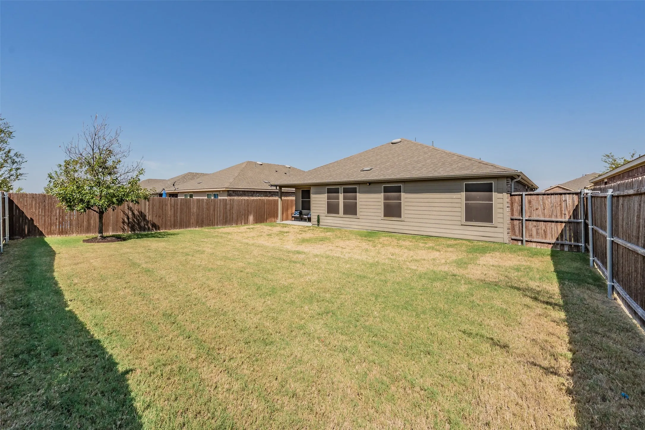 Expansive backyard featuring a manicured lawn, full privacy fencing, and a mature tree