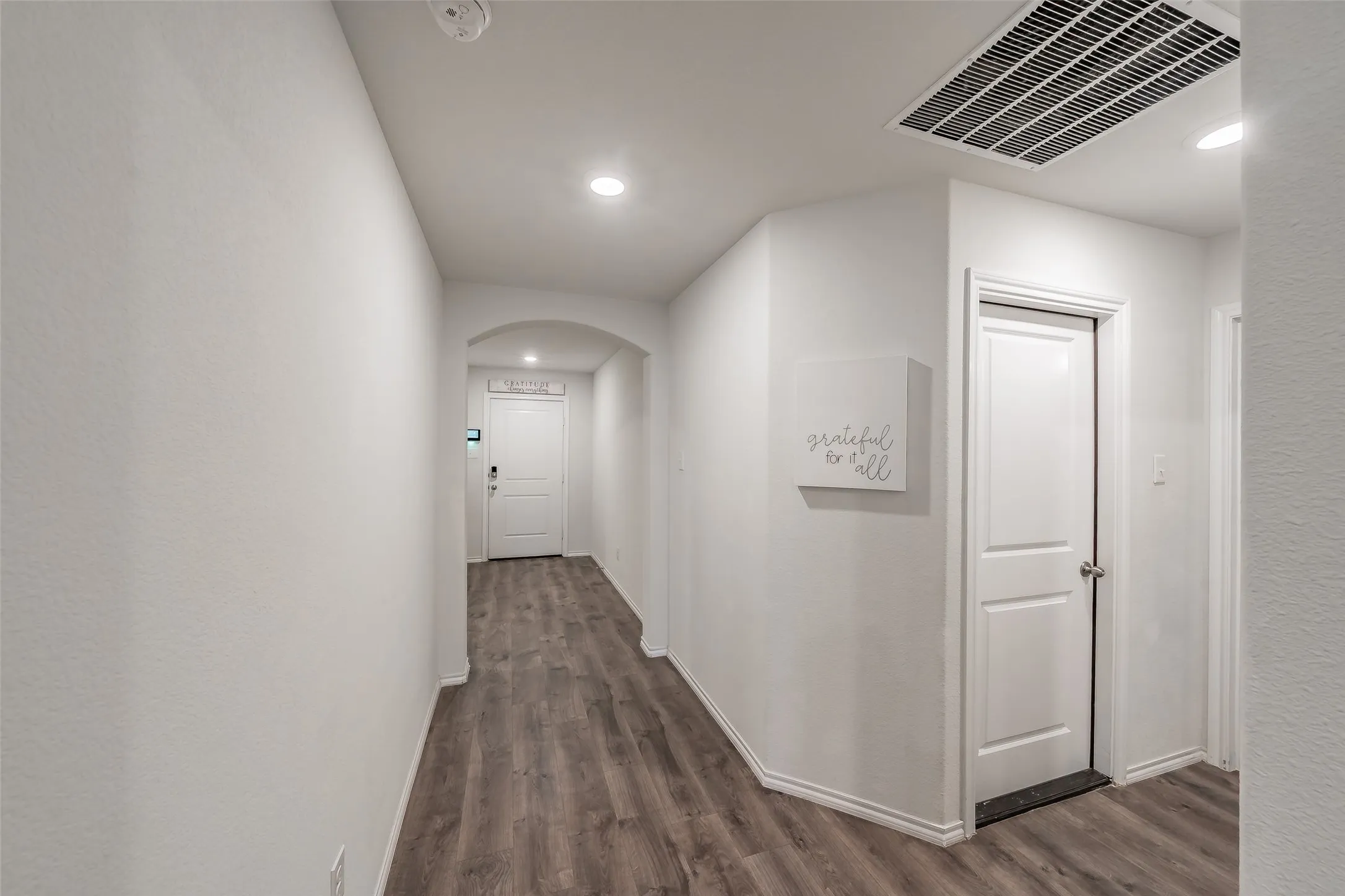 Hallway featuring wood-finish flooring, recessed lighting, white walls, and a white paneled door