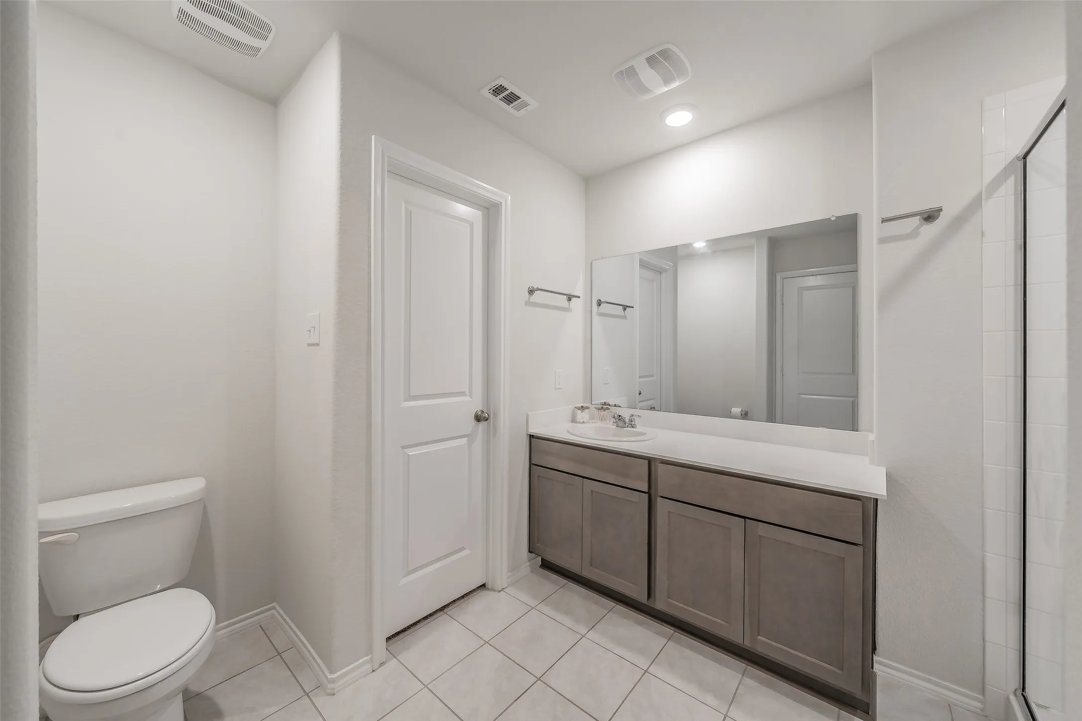 White tile flooring with a large vanity featuring double cabinets, a light countertop, and a single basin sink