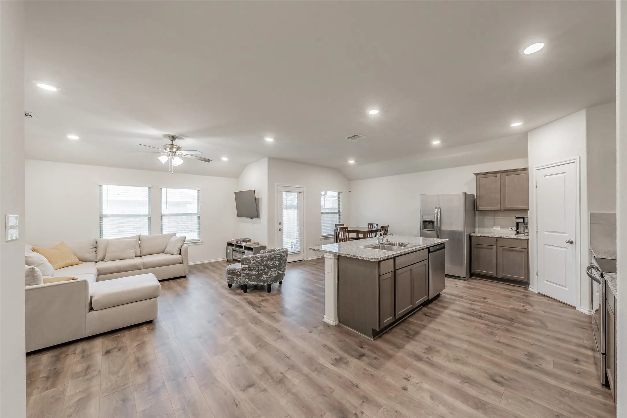 Open-concept living area with wood-finish flooring, vaulted ceiling, and recessed lighting