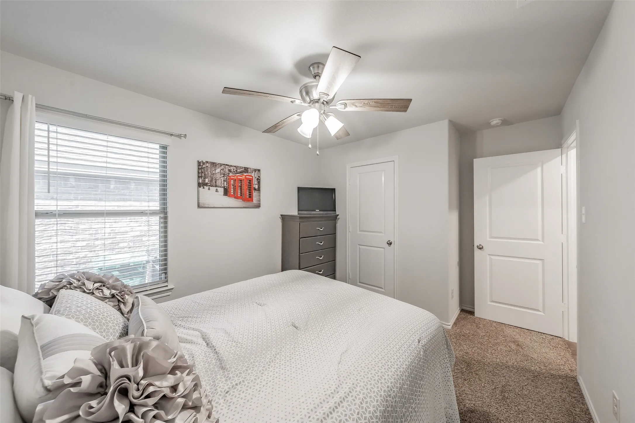 Carpeted bedroom being used as an office with a single window, overhead lighting, and a white door