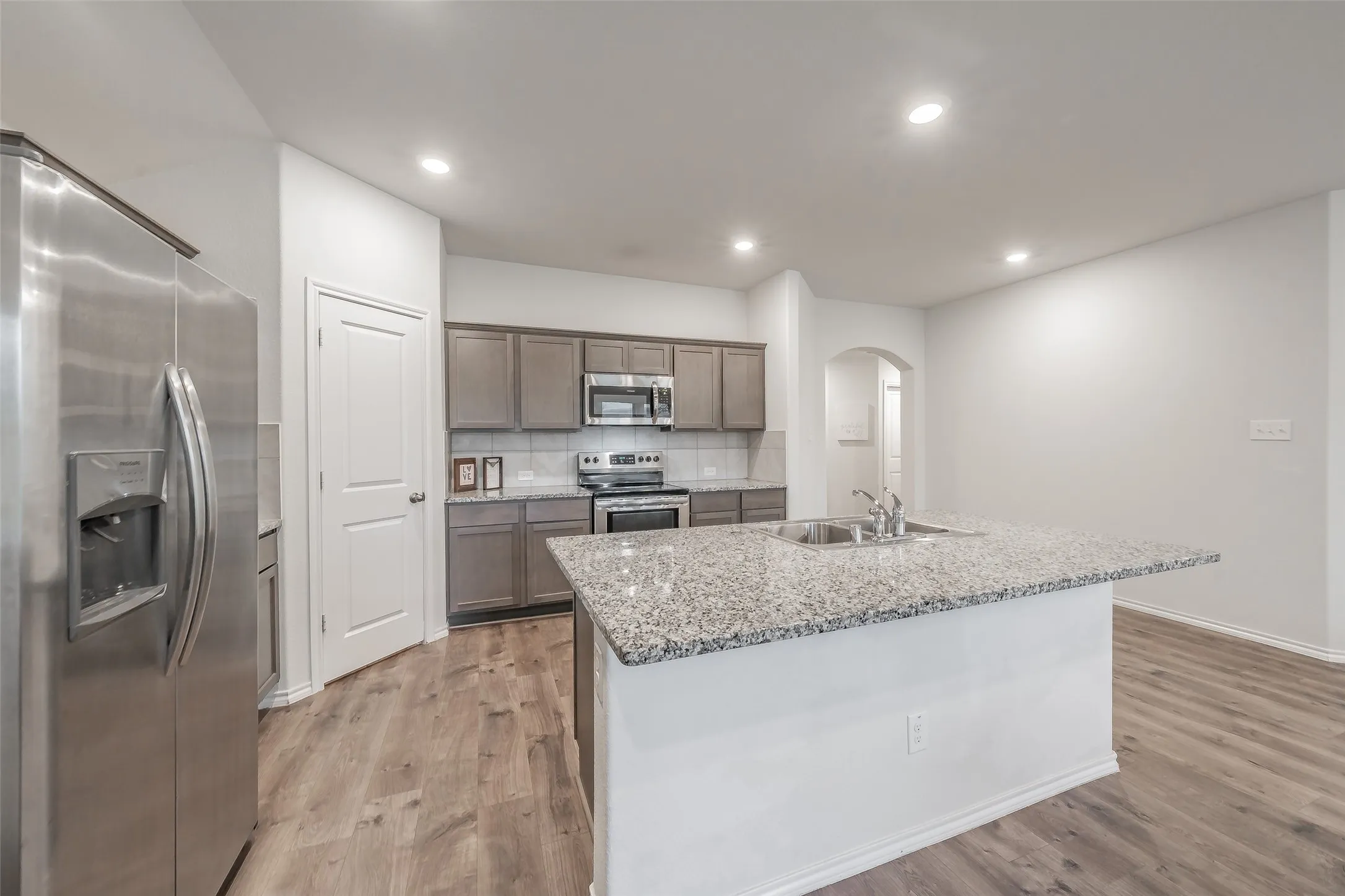 Kitchen featuring a central island with an undermount sink, wood-finish flooring, stainless steel appliances, recessed lighting, and a tile backsplash