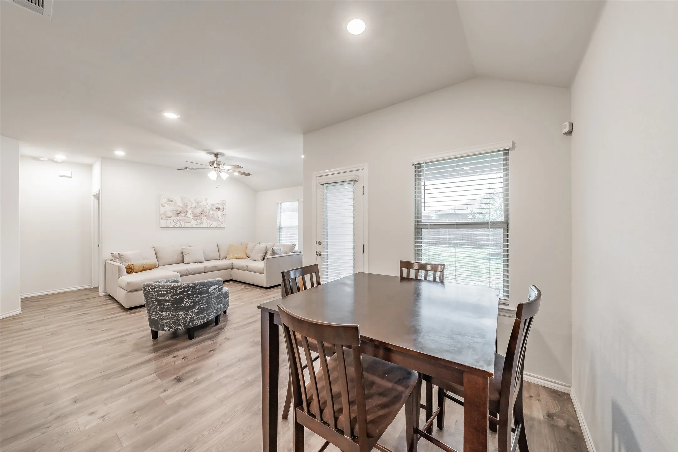 Vaulted ceiling with recessed lighting, wood-finish flooring, white walls, and a window with blinds