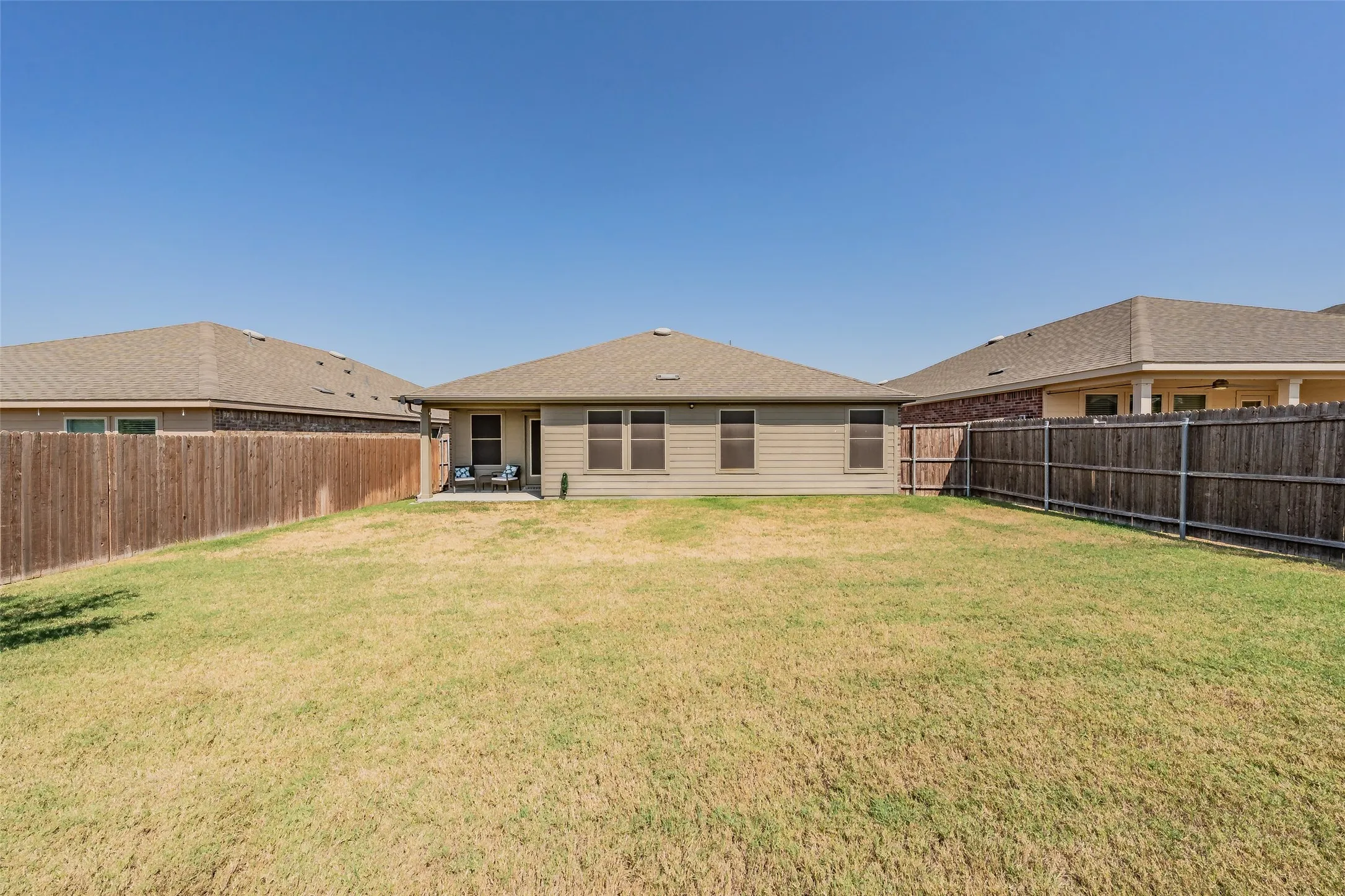 Expansive backyard featuring a wood fence perimeter and a covered patio area
