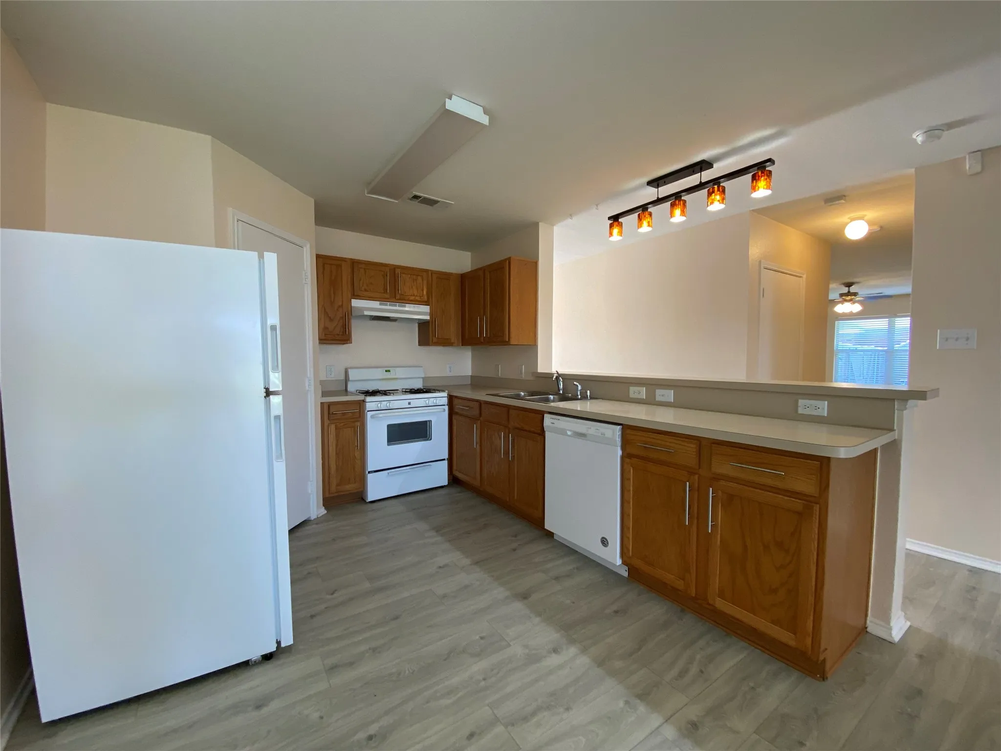 Kitchen featuring white appliances, under cabinet range hood, a sink, a peninsula, and brown cabinets