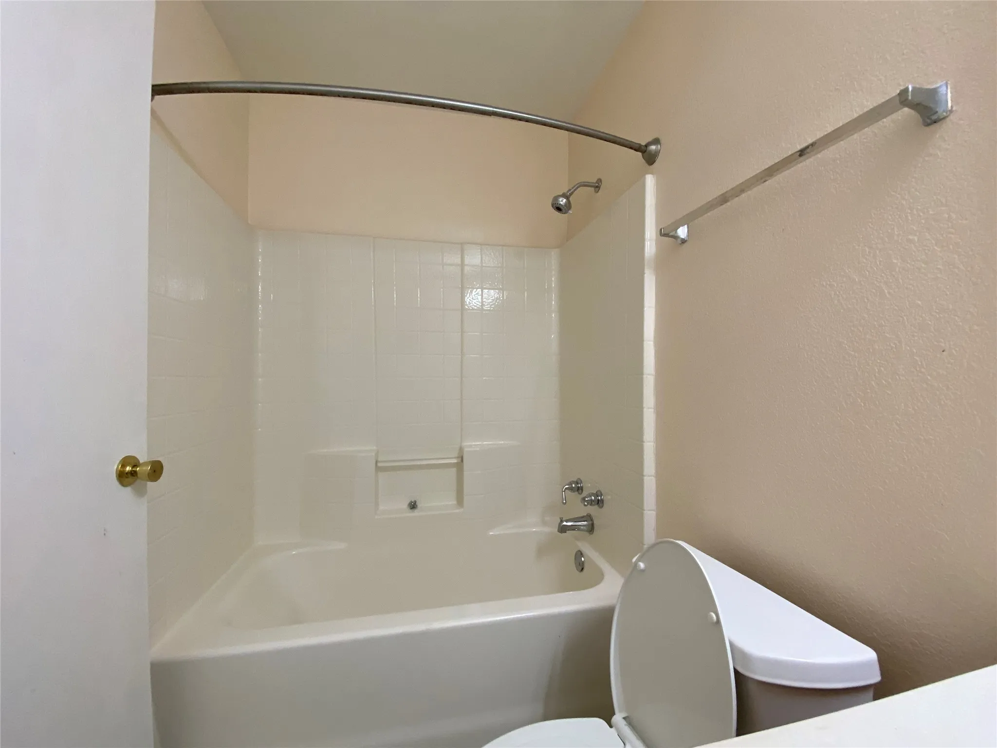 Bathroom featuring toilet, a textured wall, and  shower combination