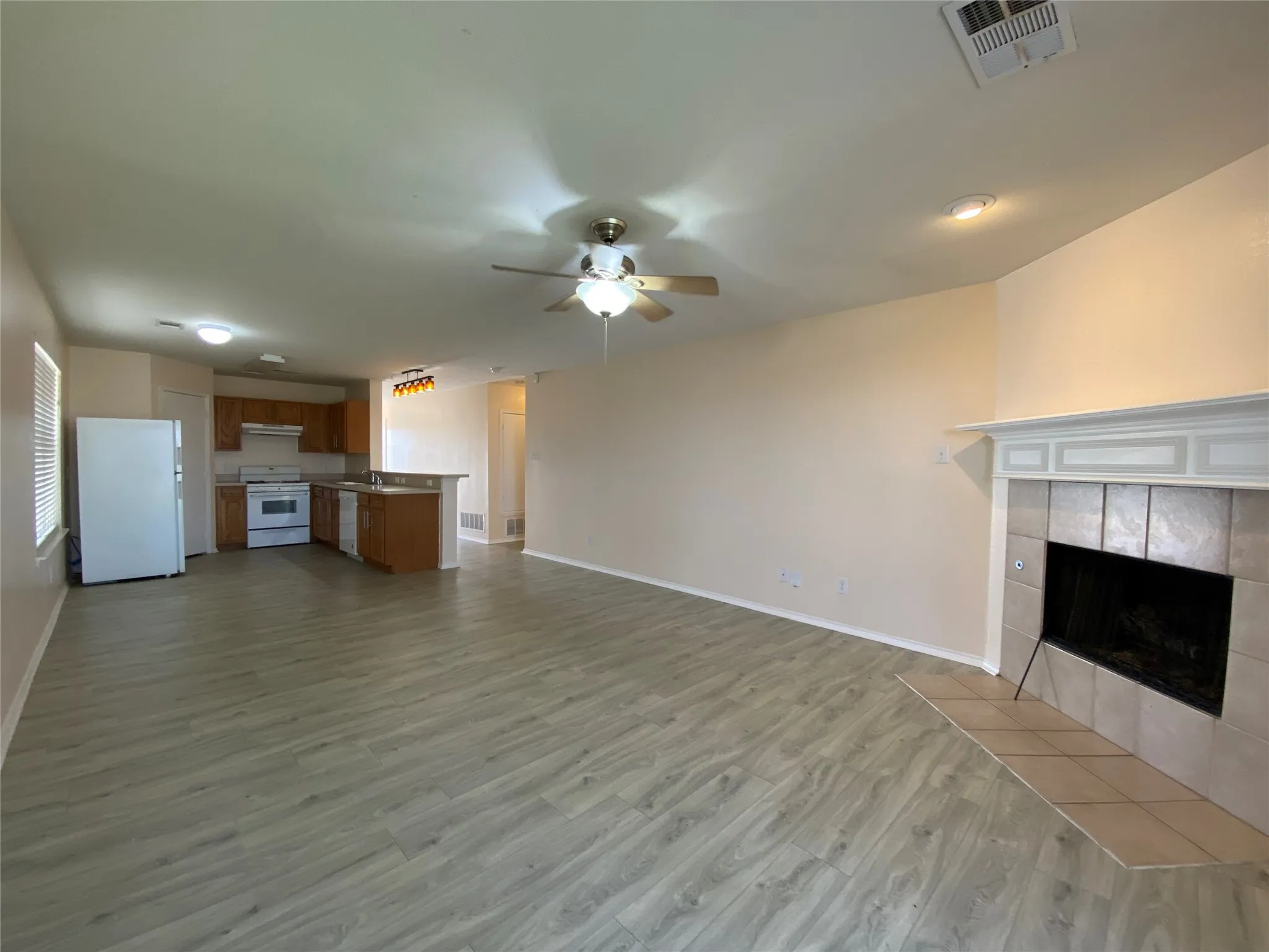 Unfurnished living room featuring baseboards, ceiling fan, a tiled fireplace, visible vents, and wood finished floors