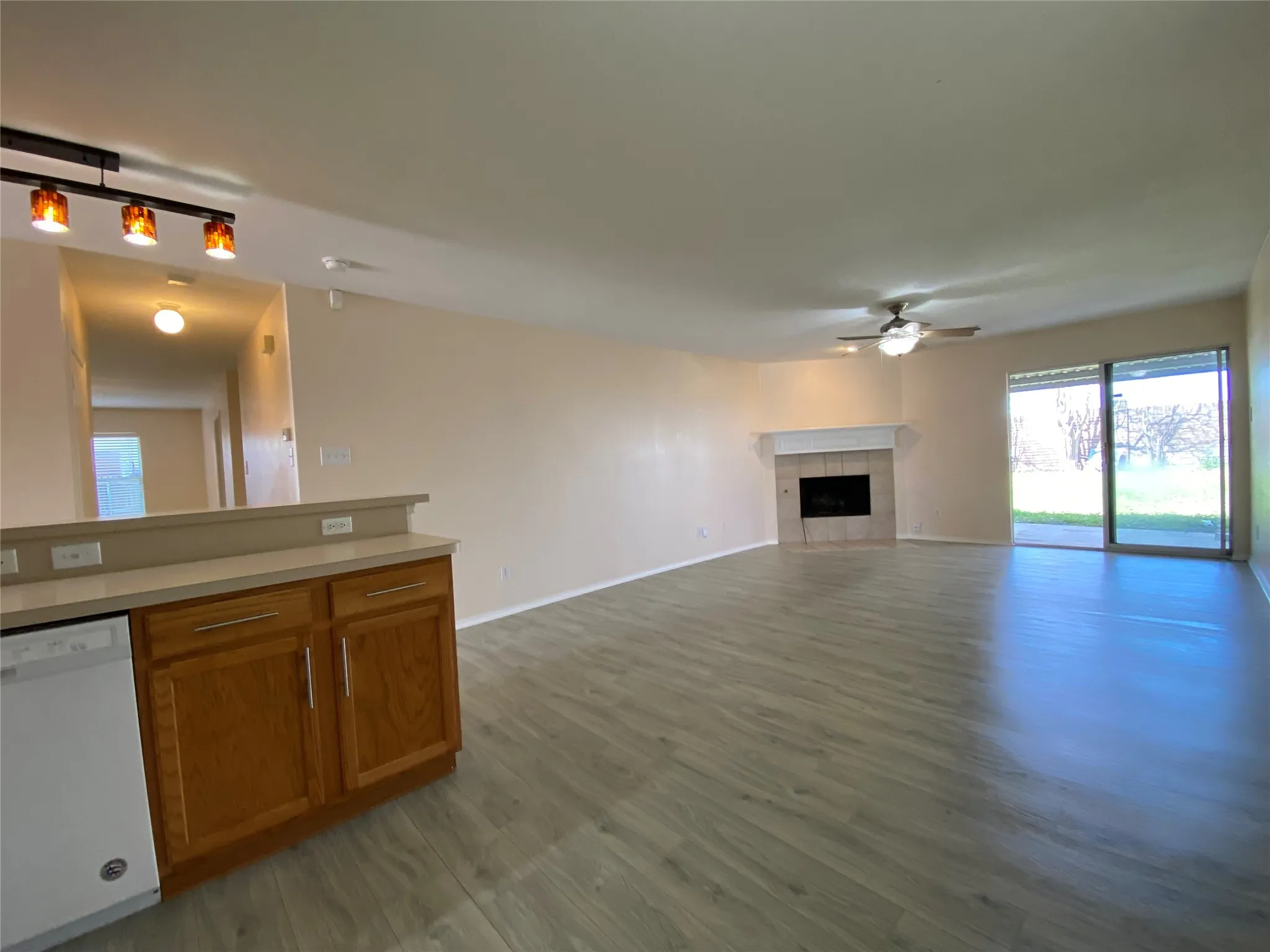 Unfurnished living room featuring a ceiling fan, a tile fireplace, baseboards, and wood finished floors