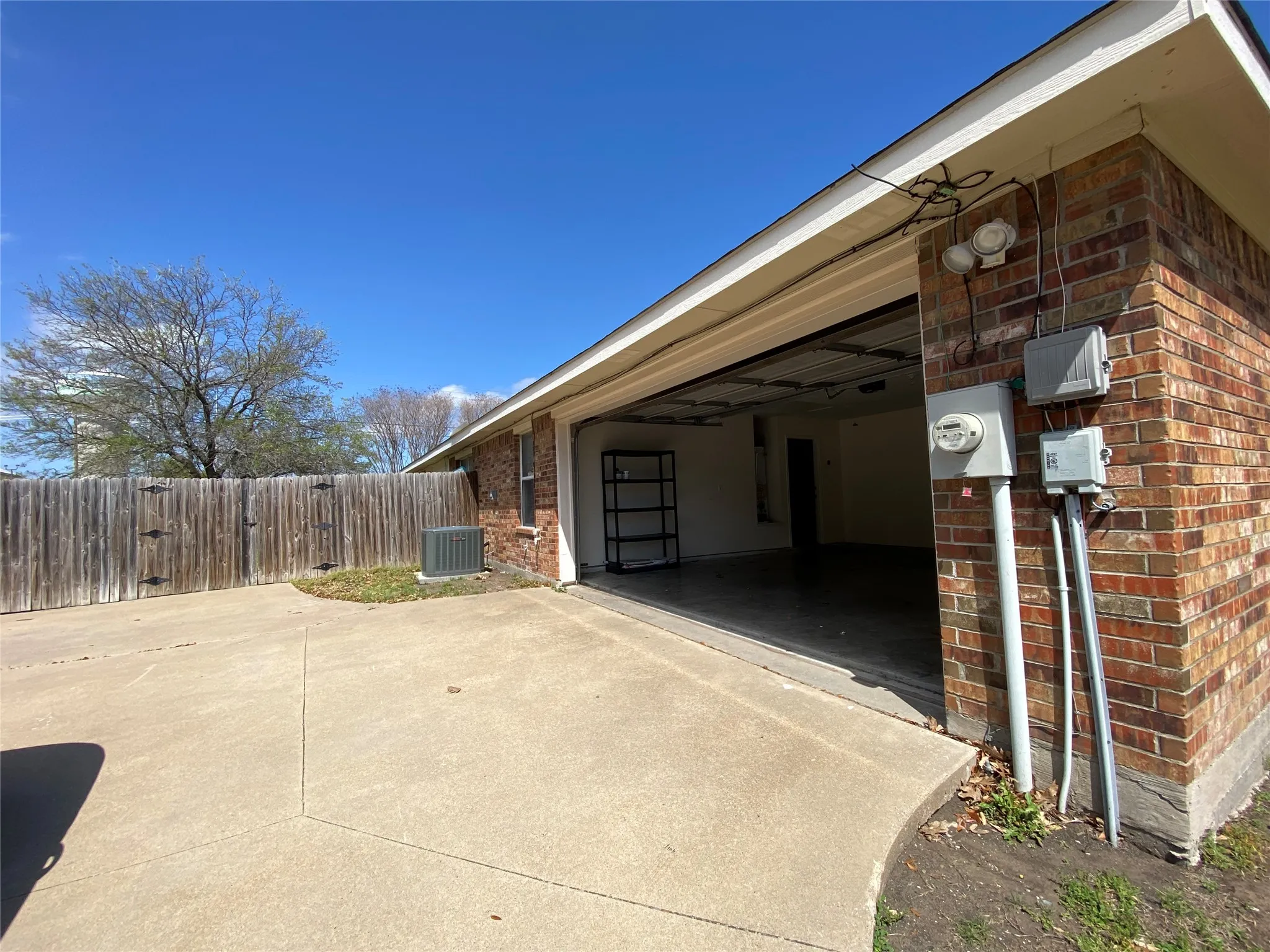View of side of home with driveway, cooling unit, an attached garage, fence, and brick siding