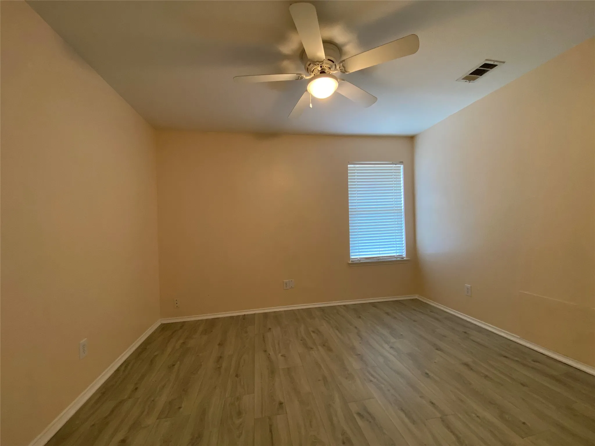Spare room with a ceiling fan, visible vents, baseboards, and wood finished floors