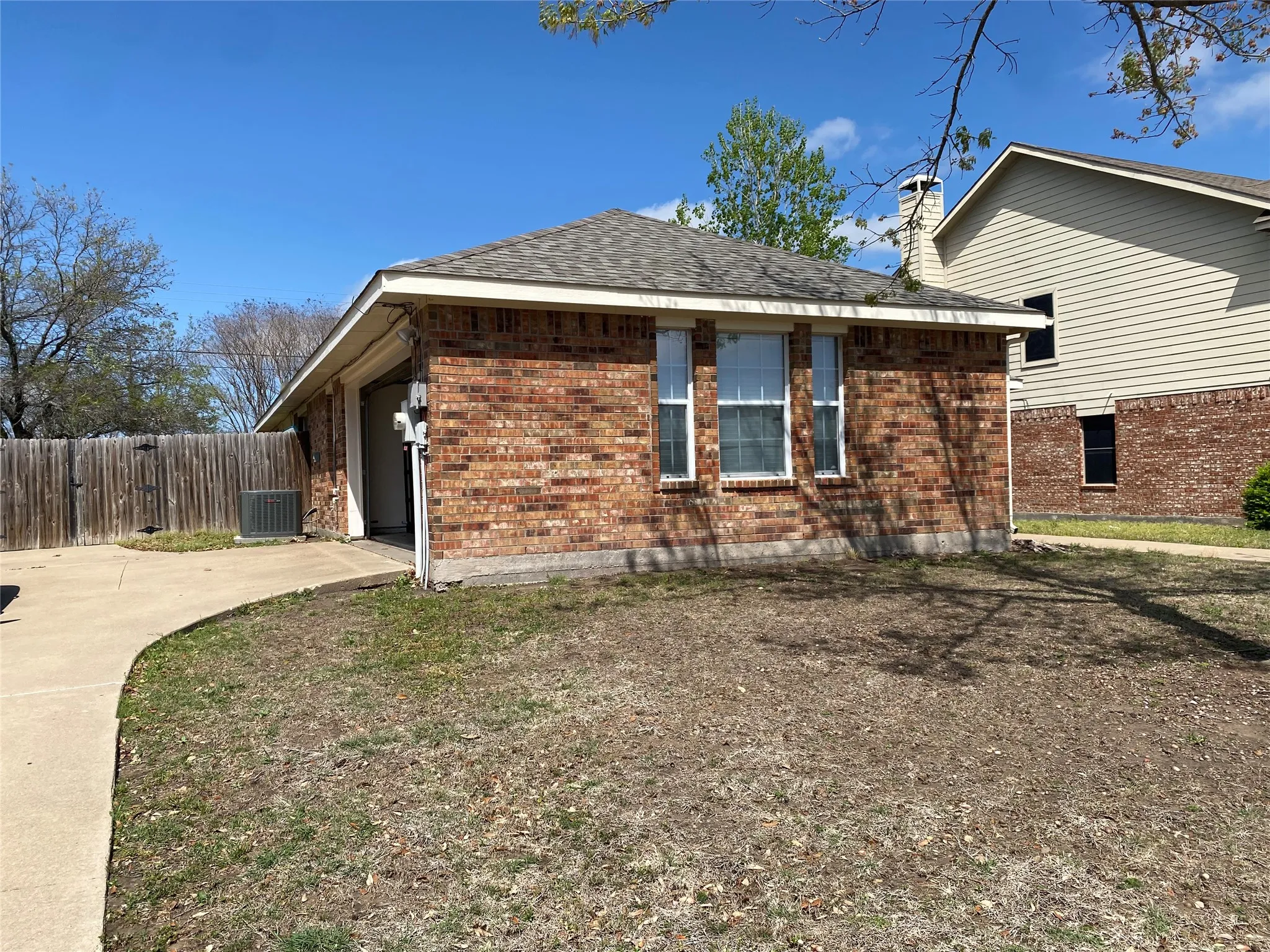 View of side of home with fence, a chimney, central AC, brick siding, and roof with shingles