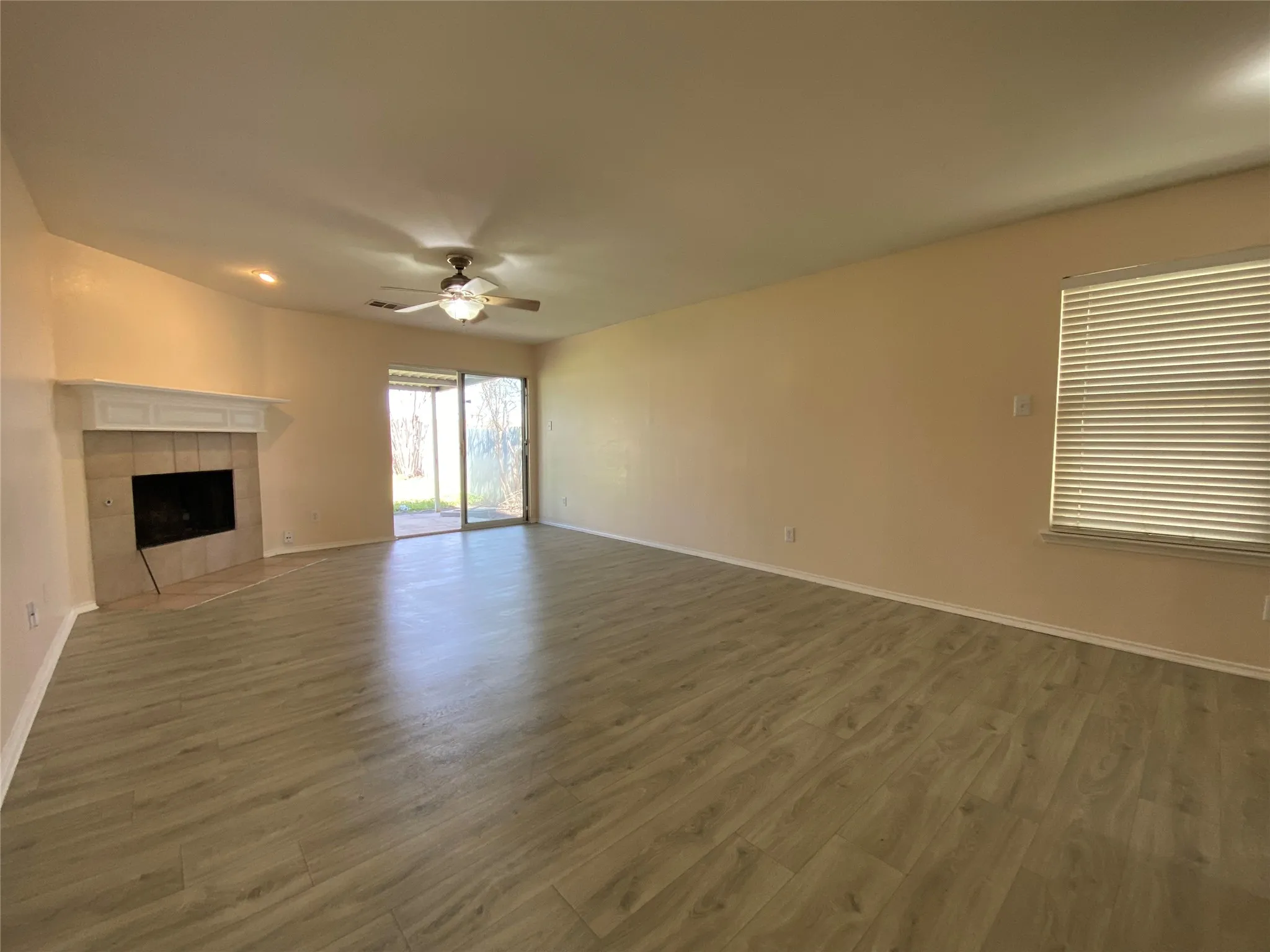 Unfurnished living room featuring wood finished floors, a tile fireplace, baseboards, and ceiling fan