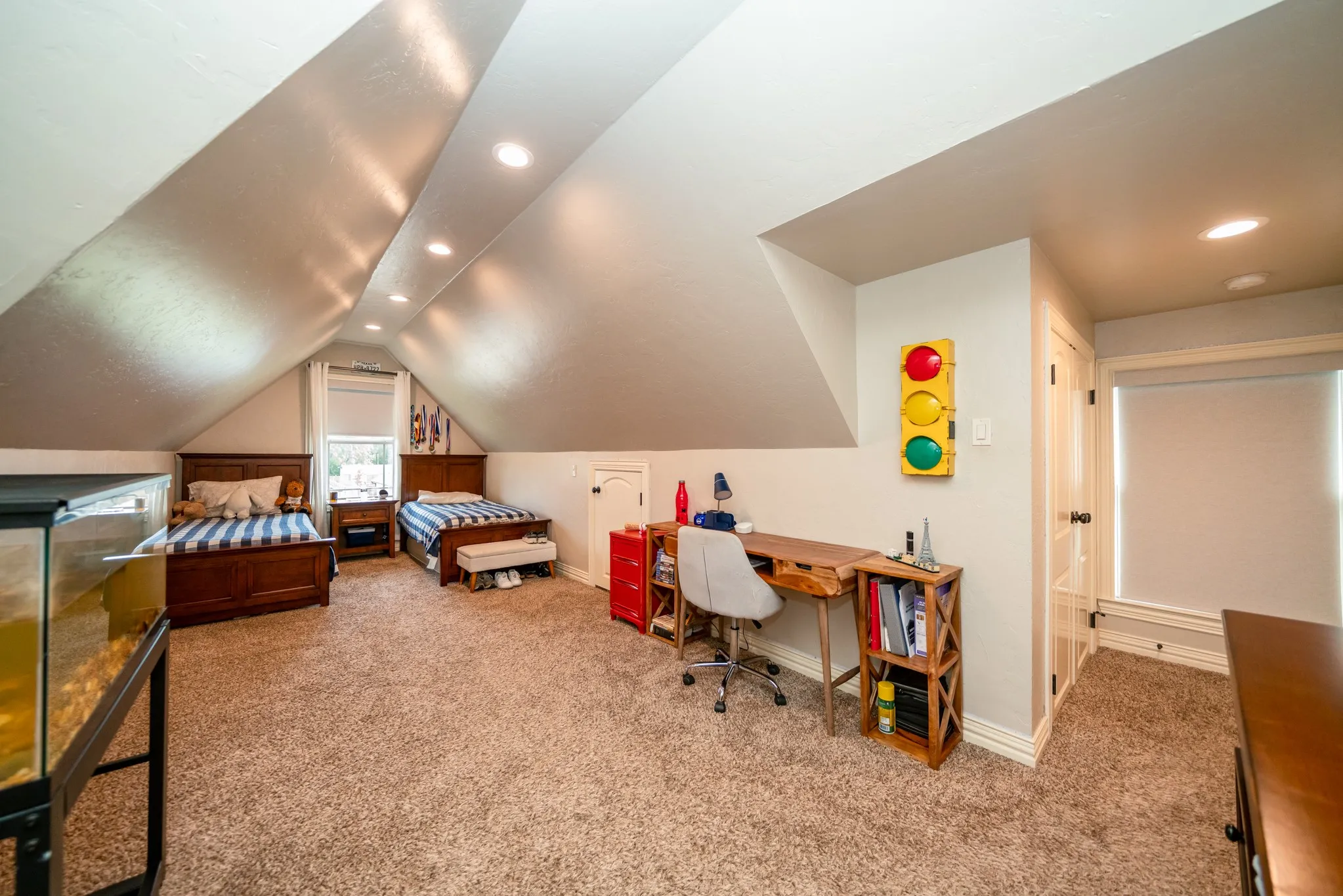 Sloped ceilings with recessed lighting, light brown carpeting, a built-in storage area, and a white door leading to an additional space
