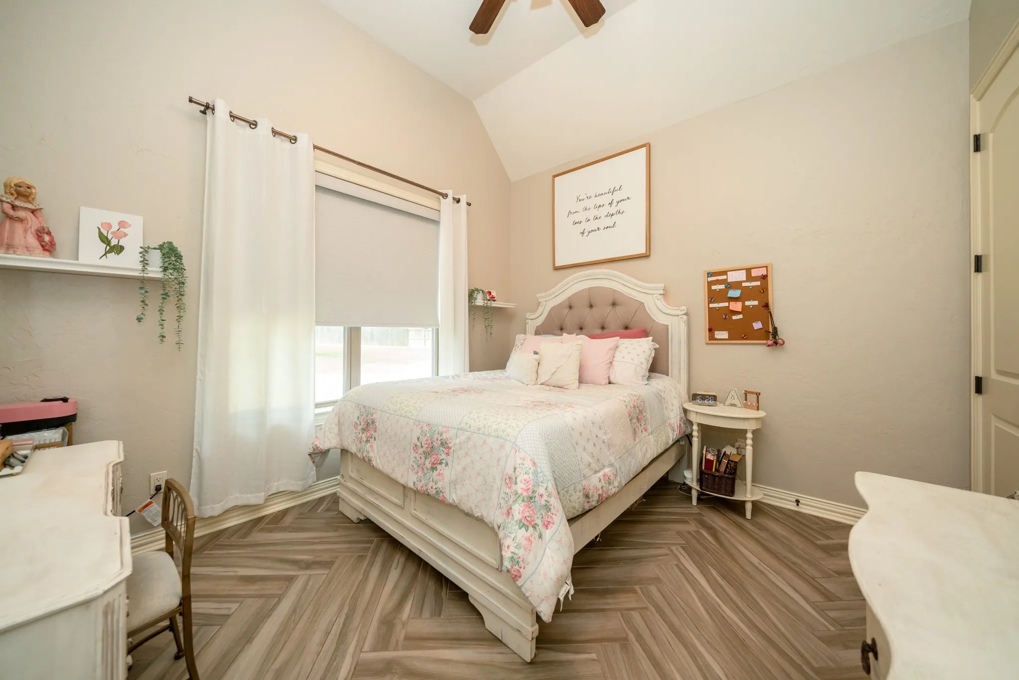 Vaulted ceiling with a ceiling fan, window with roller shade, wood-finish flooring in a herringbone pattern, and built-in wall shelving