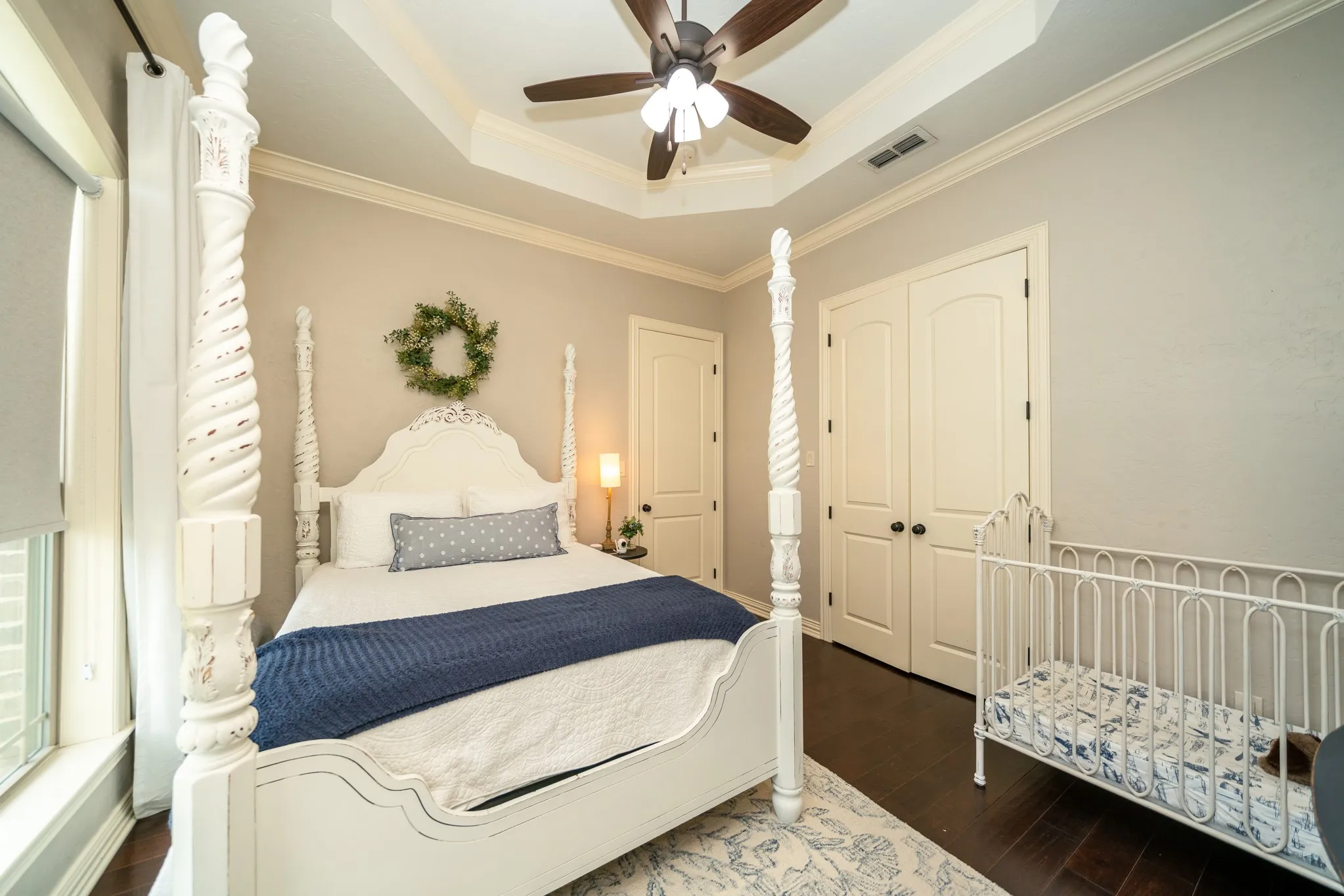 Tray ceiling with crown molding, dark wood-finish flooring, two panel doors, and a ceiling fan with integrated lighting