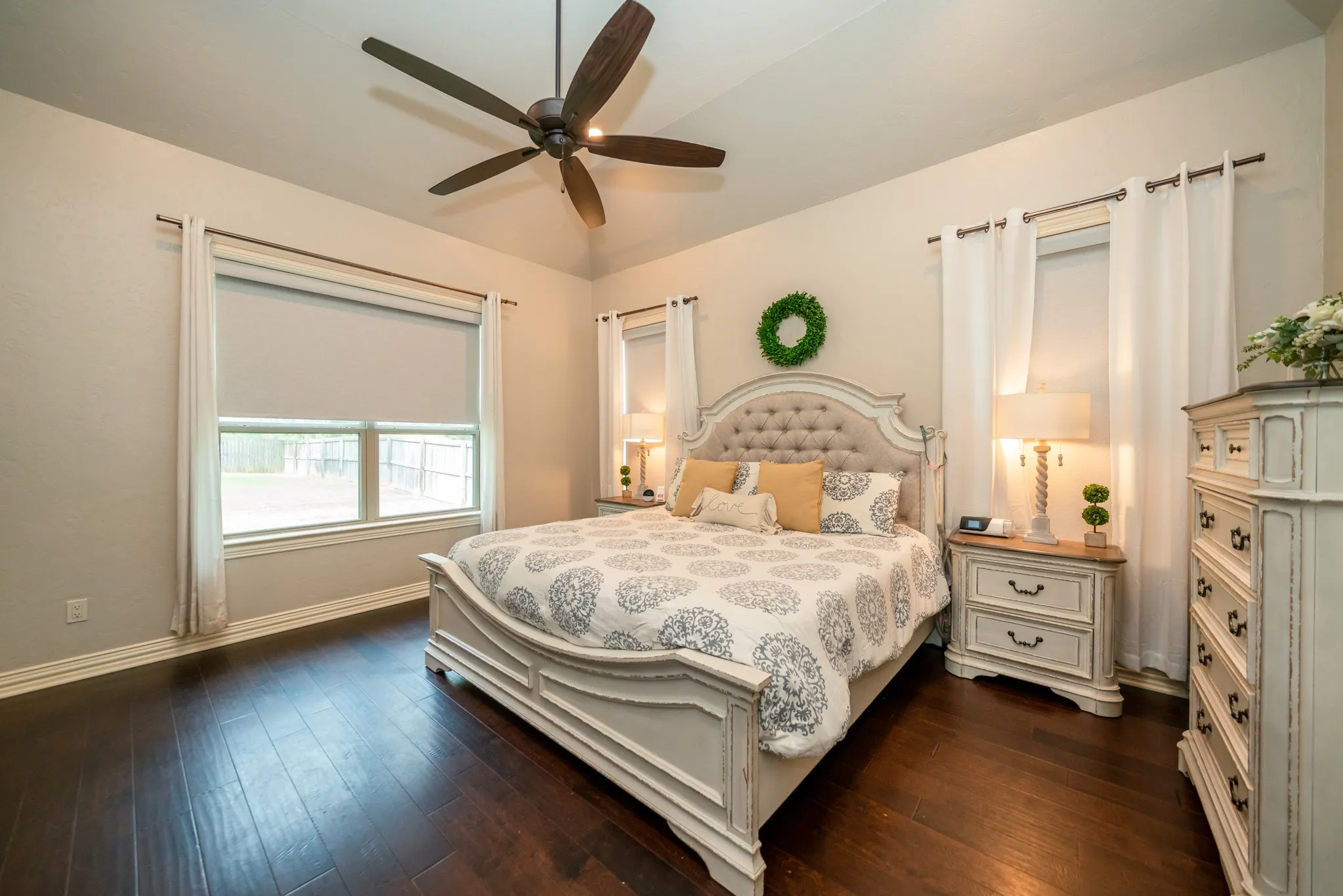 Vaulted ceiling with a ceiling fan, dark wood-finish flooring, and multiple windows with roller shades