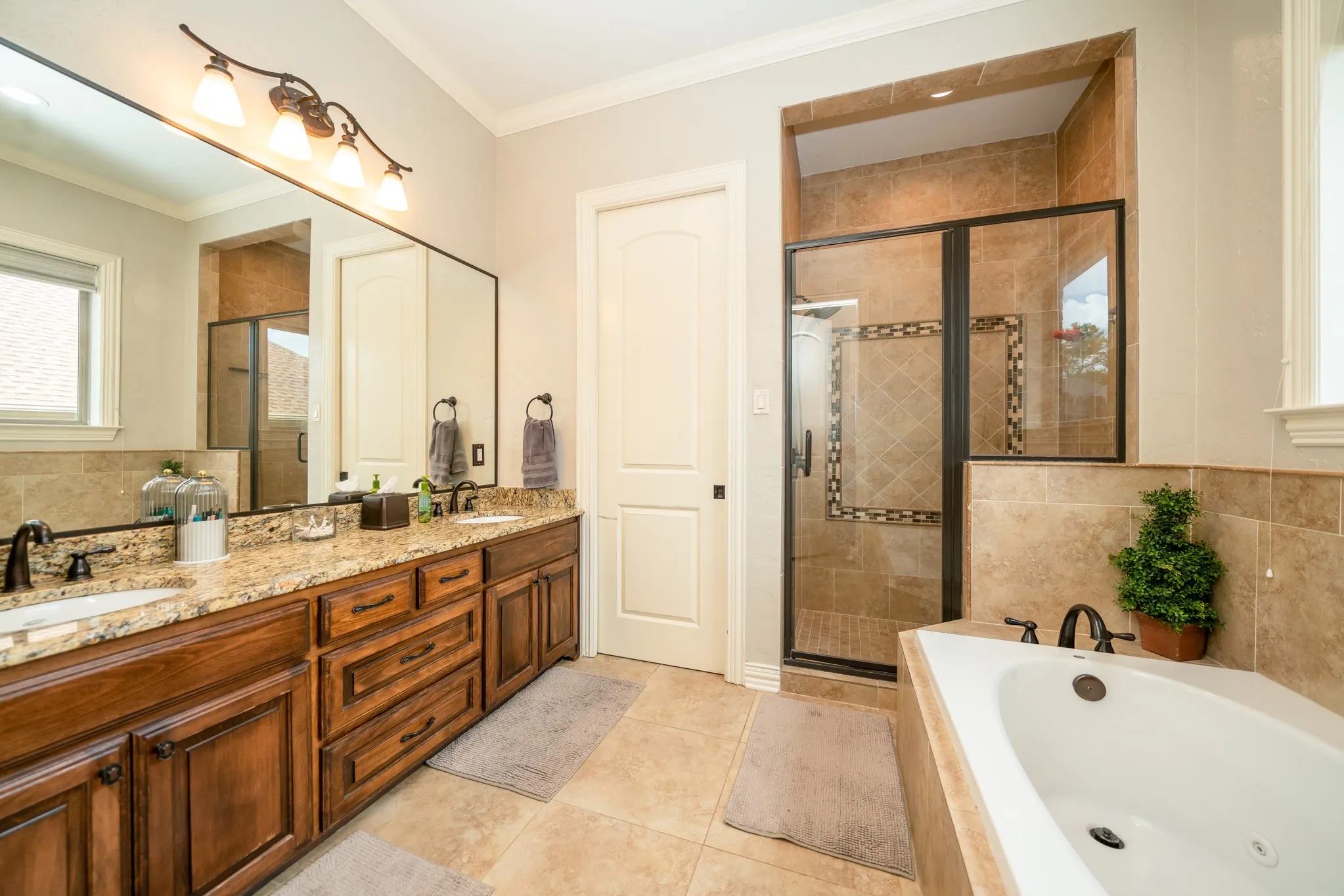 Dual-sink vanity with wood-finish cabinetry, granite countertop, and integrated corner bathtub