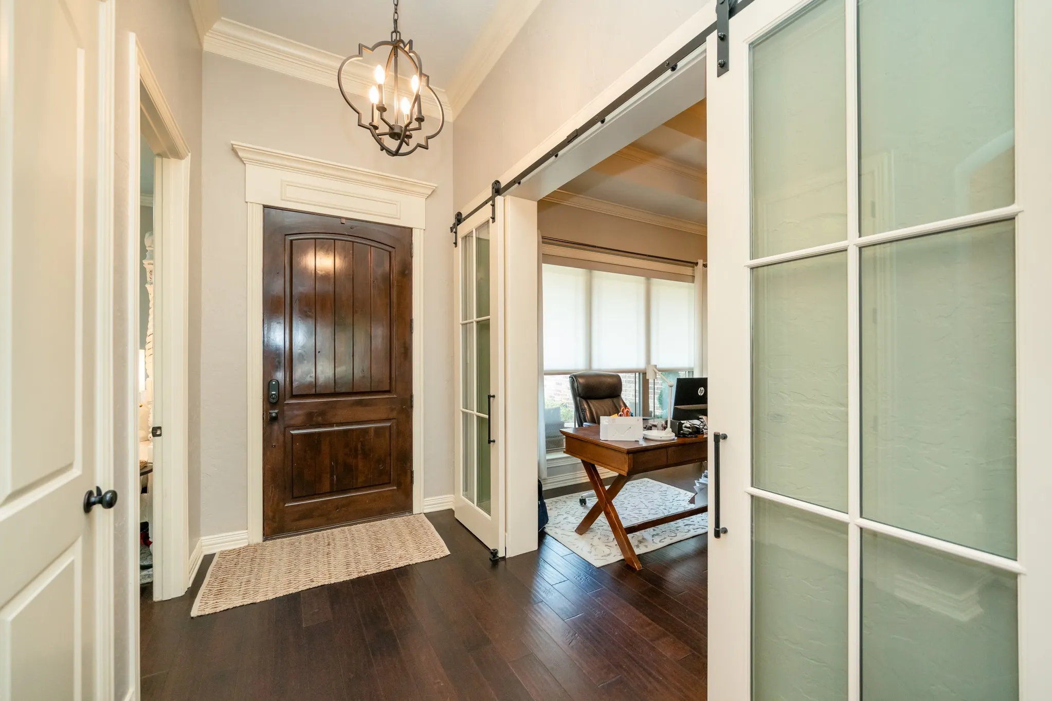 Arched entry door with dark wood finish, dark wood-finish flooring, decorative chandelier, and sliding barn doors with frosted glass panels