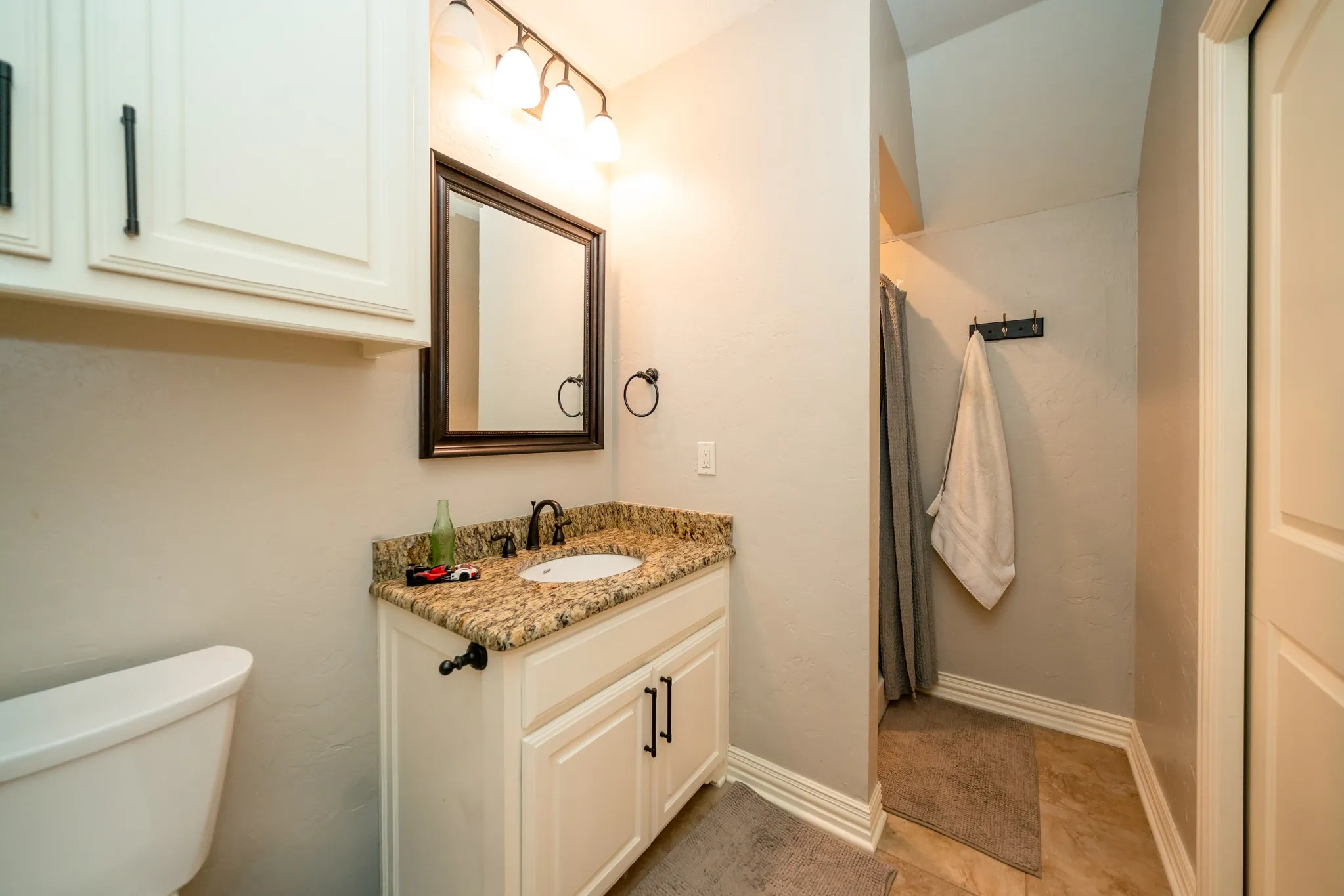 Granite-style countertop with integrated sink, white cabinetry with dark hardware, framed vanity mirror, and overhead vanity lighting