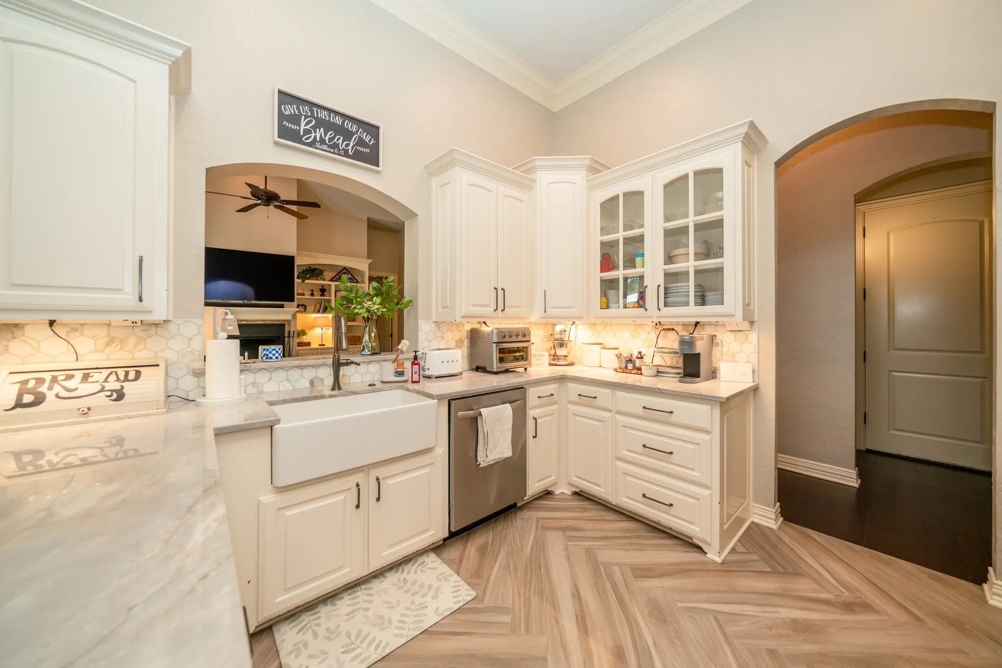 White cabinetry with glass-front accents, modern farmhouse sink, herringbone wood-finish flooring, and arched entryway