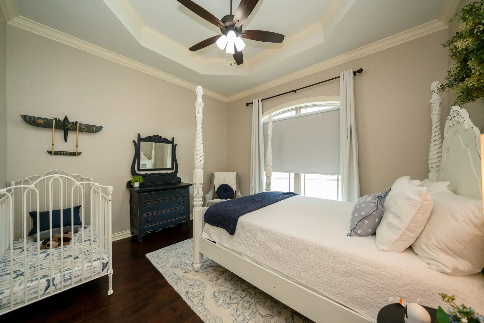 Tray ceiling with crown molding, dark wood-finish flooring, arched window, and ceiling fan with lighting