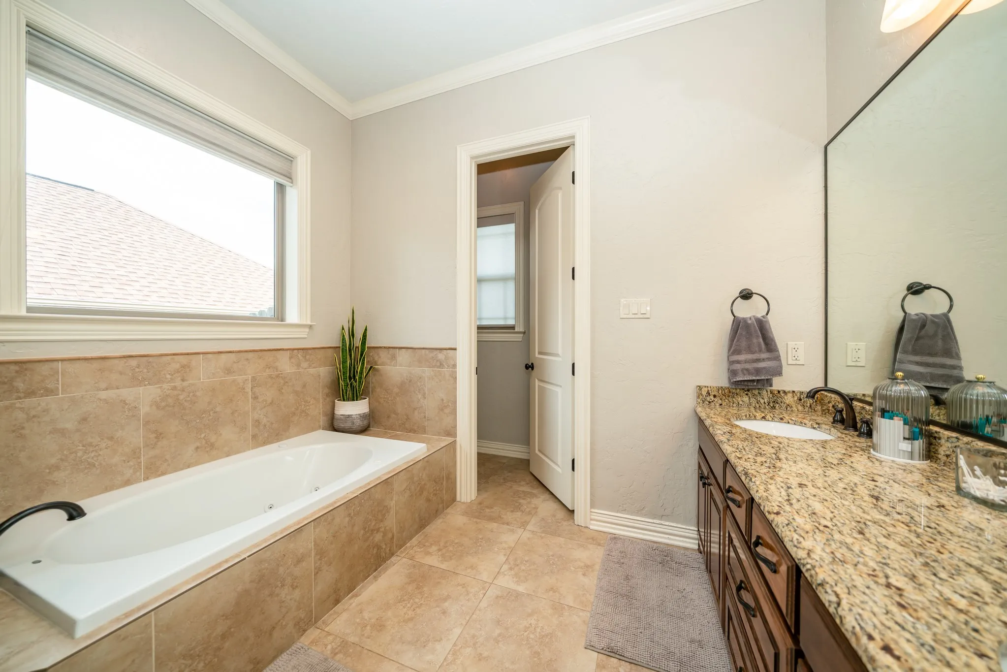 Soaking tub with tile surround, dual sink vanity with stone countertop, and tile flooring