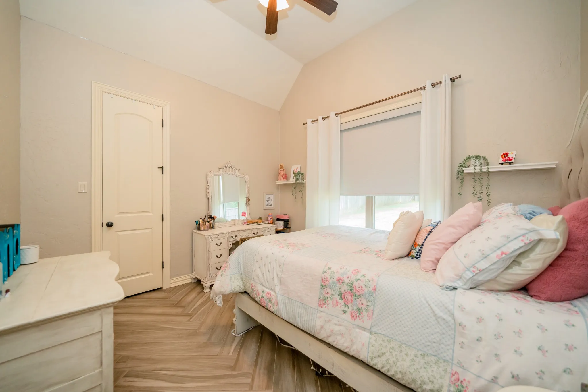 Bright secondary bedroom showcasing vaulted ceilings with ceiling fan, wood-finish flooring, and ample natural light from dual windows with cellular shades