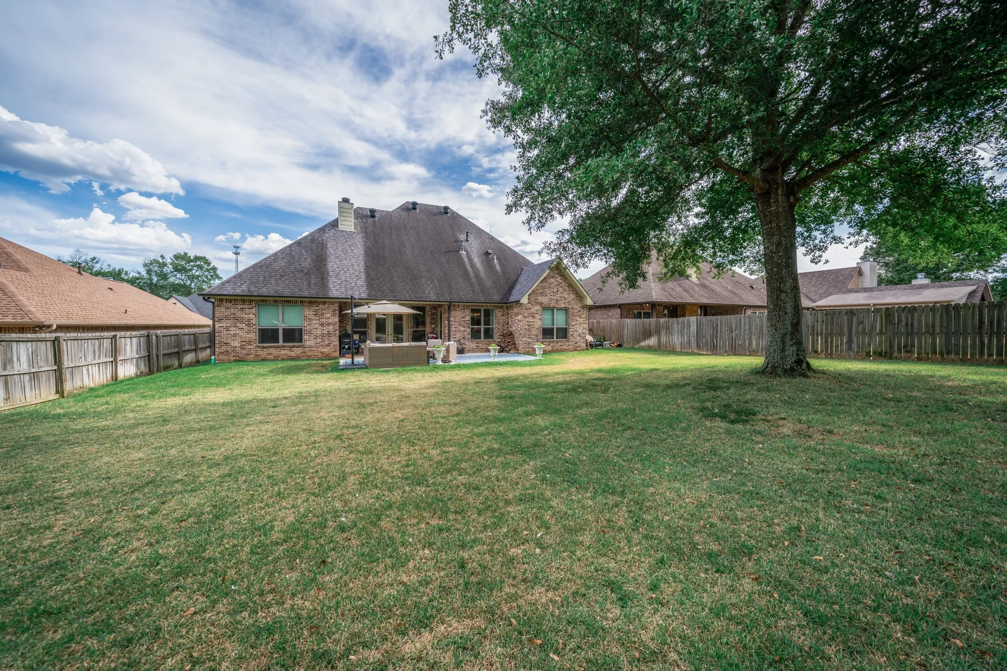 Expansive backyard featuring a manicured lawn, a mature tree, a full privacy fence, a brick exterior, and a paved patio​​‌​​​​‌​​‌‌​‌‌​​​‌‌​‌​‌​‌​​​‌​​ area