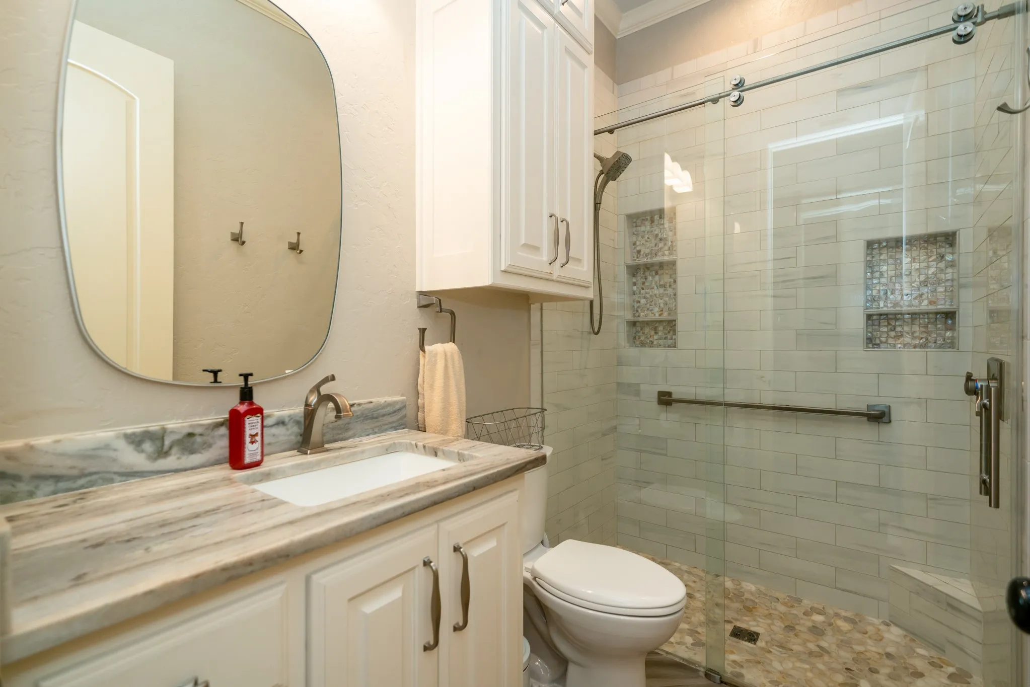 Modern bathroom featuring a vanity with an integrated sink and patterned countertop, white cabinetry, and an enclosed shower with subway tile walls and pebble-finish flooring
