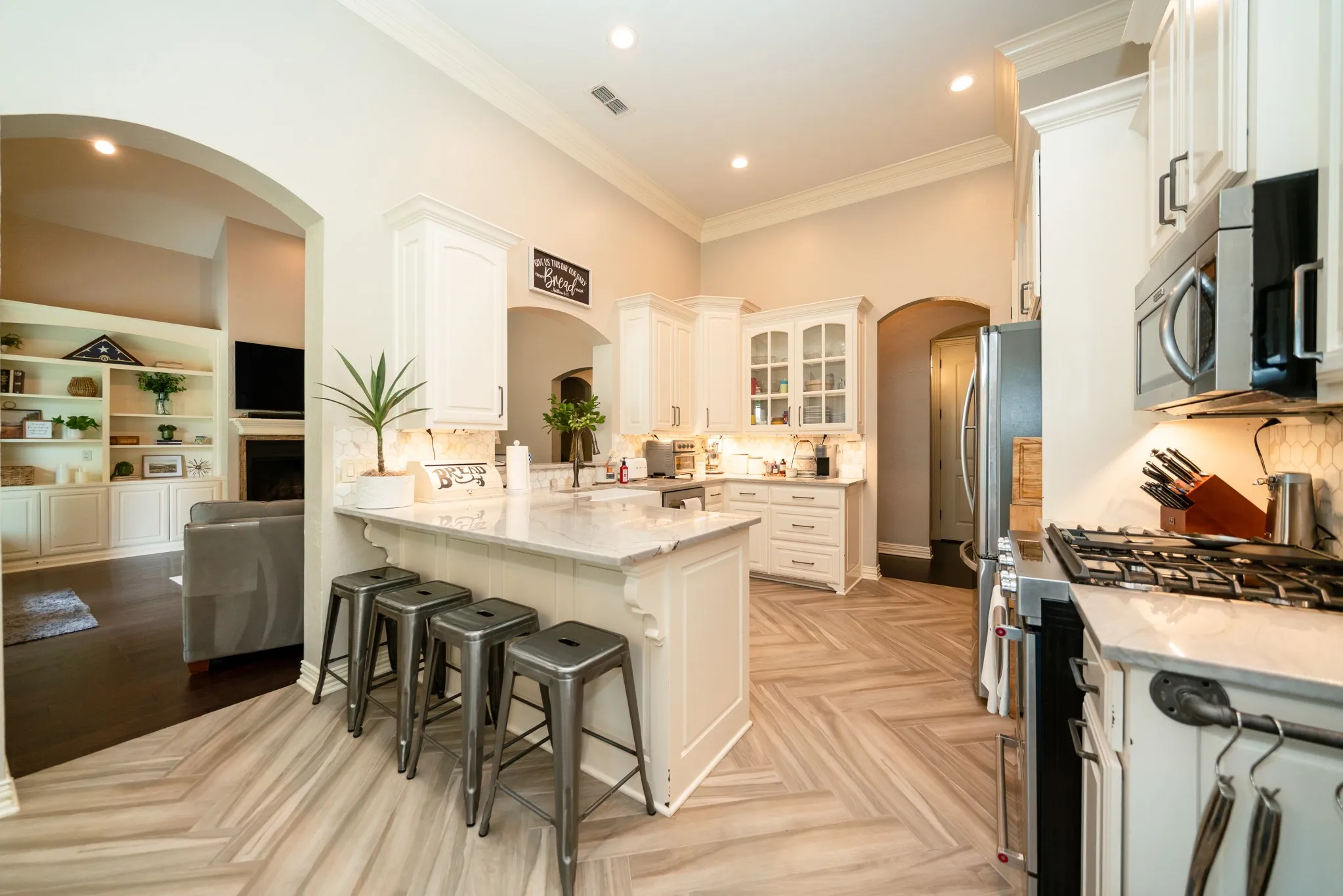 Kitchen featuring an expansive island with seating, herringbone wood-finish flooring, white cabinetry, stainless steel appliances, and recessed lighting
