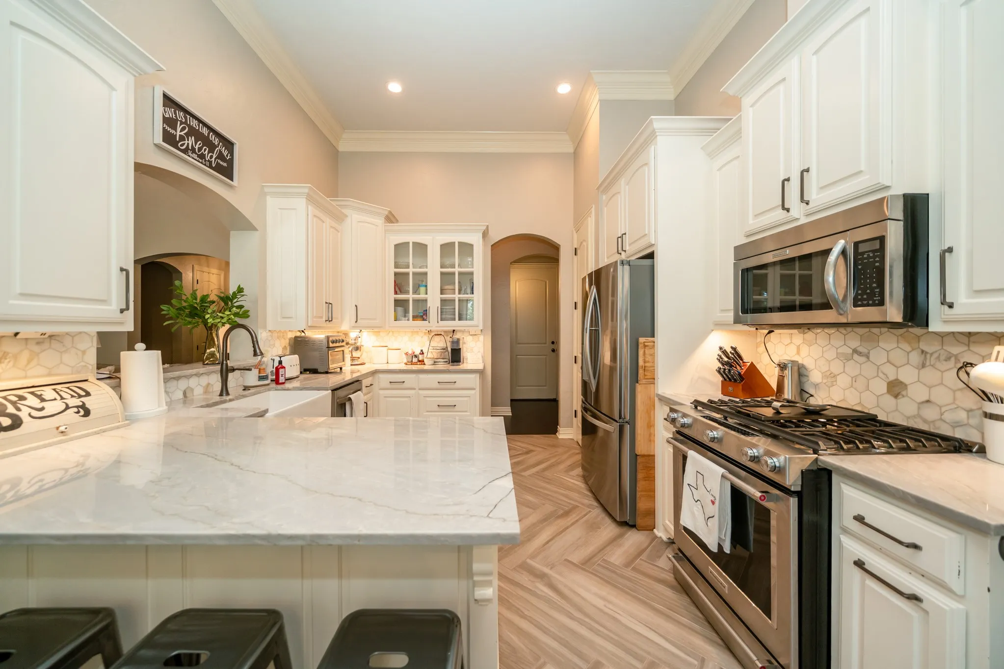 Chef's kitchen featuring white cabinetry with glass-front uppers, stainless steel appliances including a dual-fuel range, marble countertops, marble subway tile backsplash, and a large waterfall-edge island with seating for multiple guests