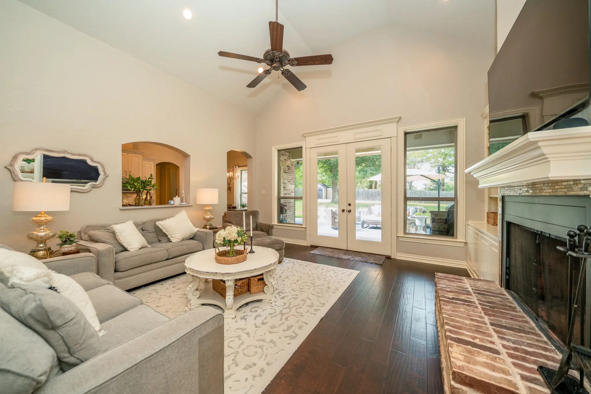 Vaulted ceilings, dark wood-finish flooring, and a fireplace with a brick hearth and stone-look surround
