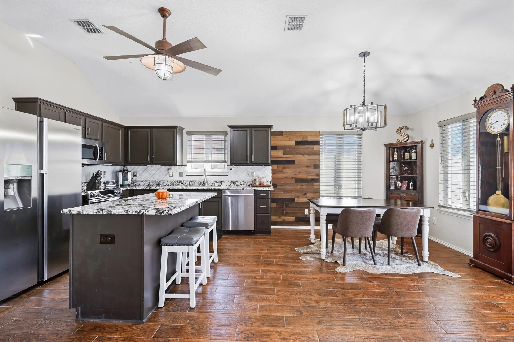 Kitchen featuring dark cabinetry, stainless steel appliances, a center island with seating, a tile backsplash, and wood-finish flooring