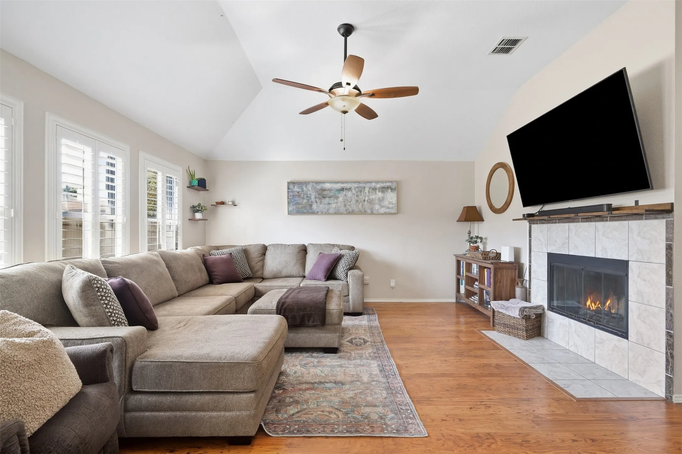Vaulted ceilings, wood-finish flooring, ceiling fan, fireplace with tile surround, and plantation shutters