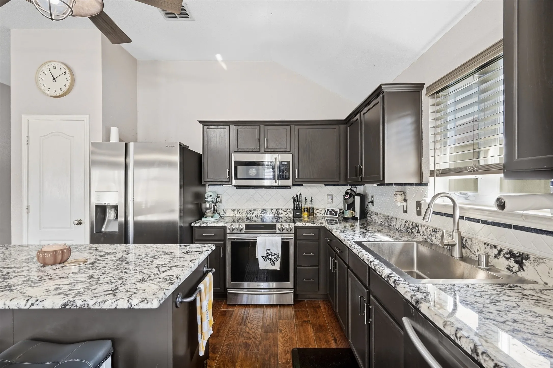 Kitchen featuring dark cabinetry, stainless steel appliances, speckled stone countertops, and wood-finish flooring