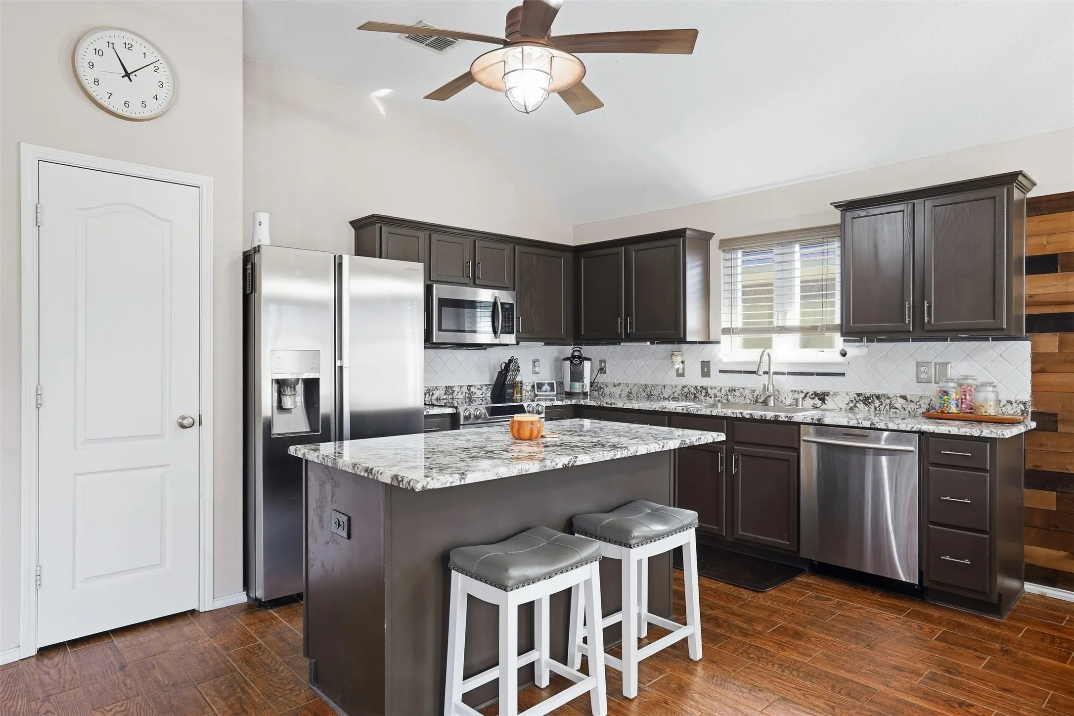 Kitchen featuring dark wood-finish cabinetry, stainless steel appliances, granite countertops, and wood-finish flooring