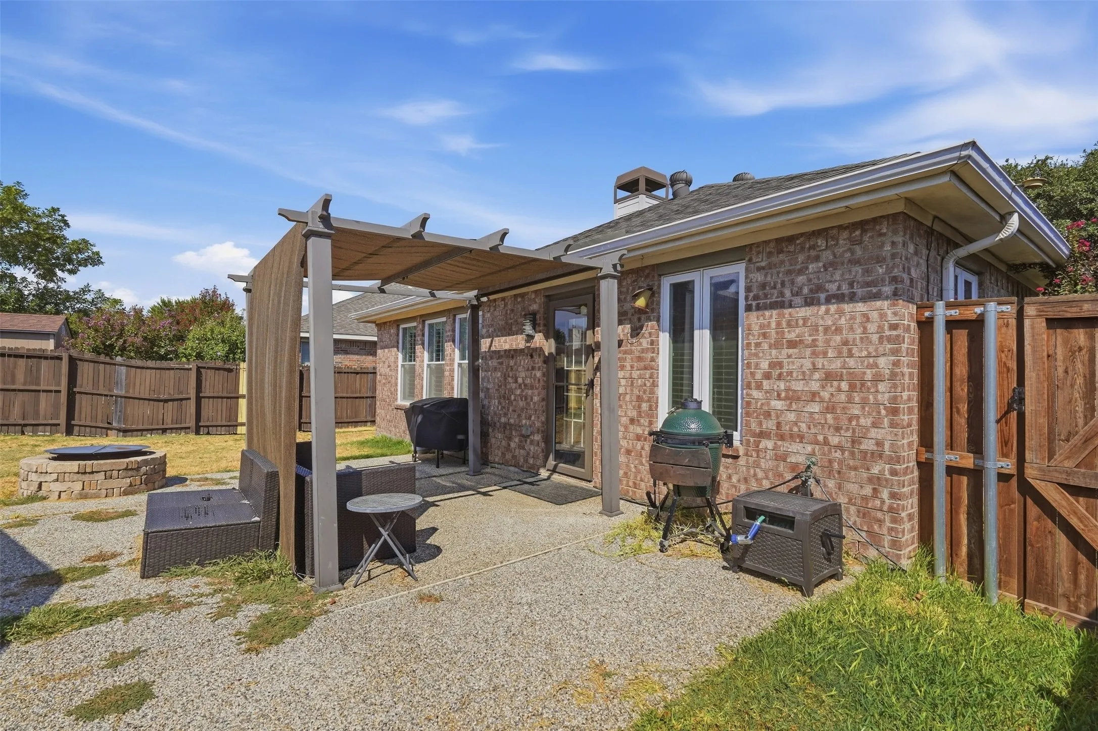 Brick exterior with a covered patio, gravel yard, wood fencing, and a built-in fire pit