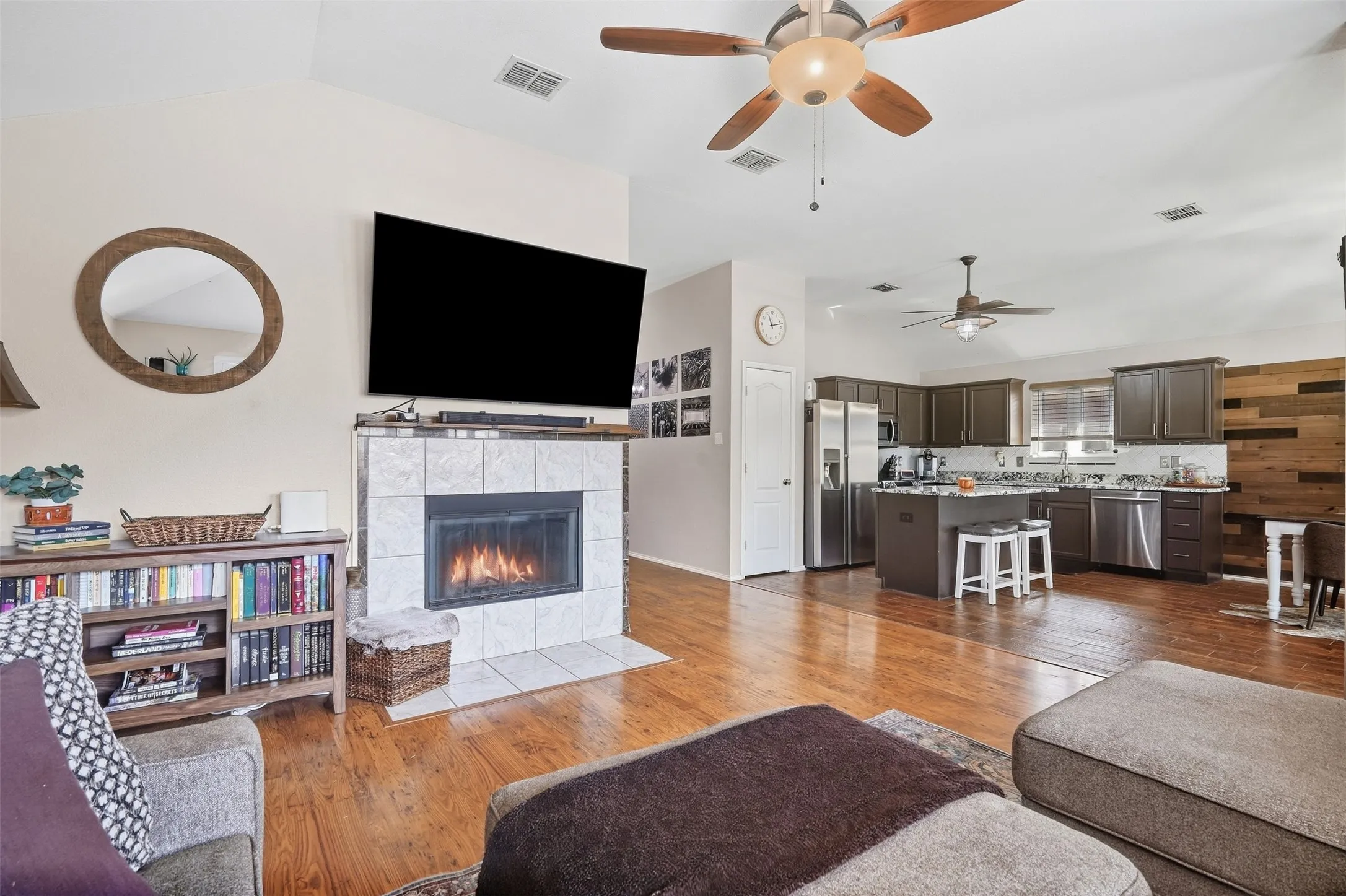 Open-concept living space featuring wood-finish flooring, a tiled fireplace, and vaulted ceilings