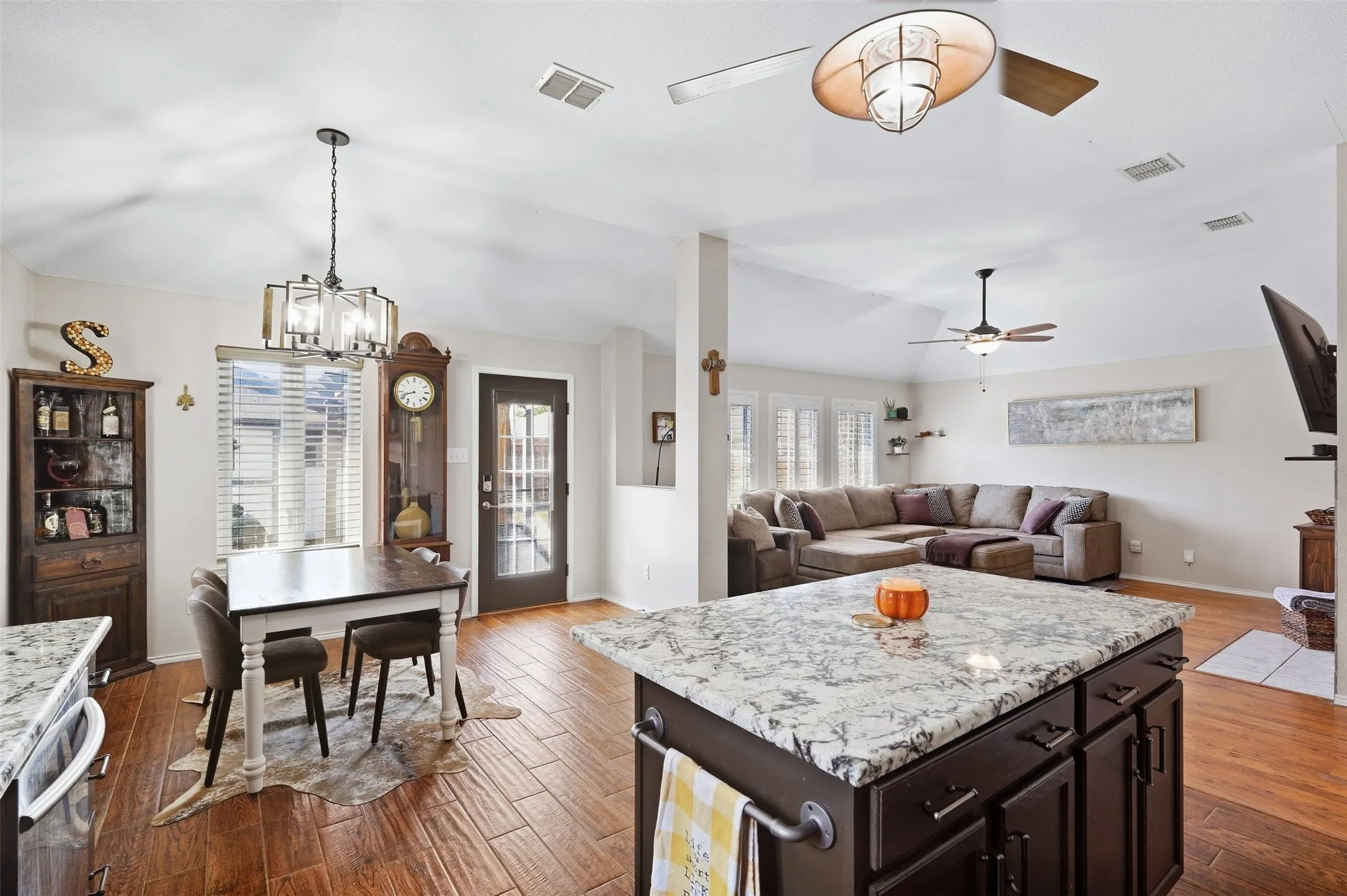 Granite-finish island with dark wood-finish cabinetry, wood-finish flooring, vaulted ceiling, and built-in ceiling fan with light fixture