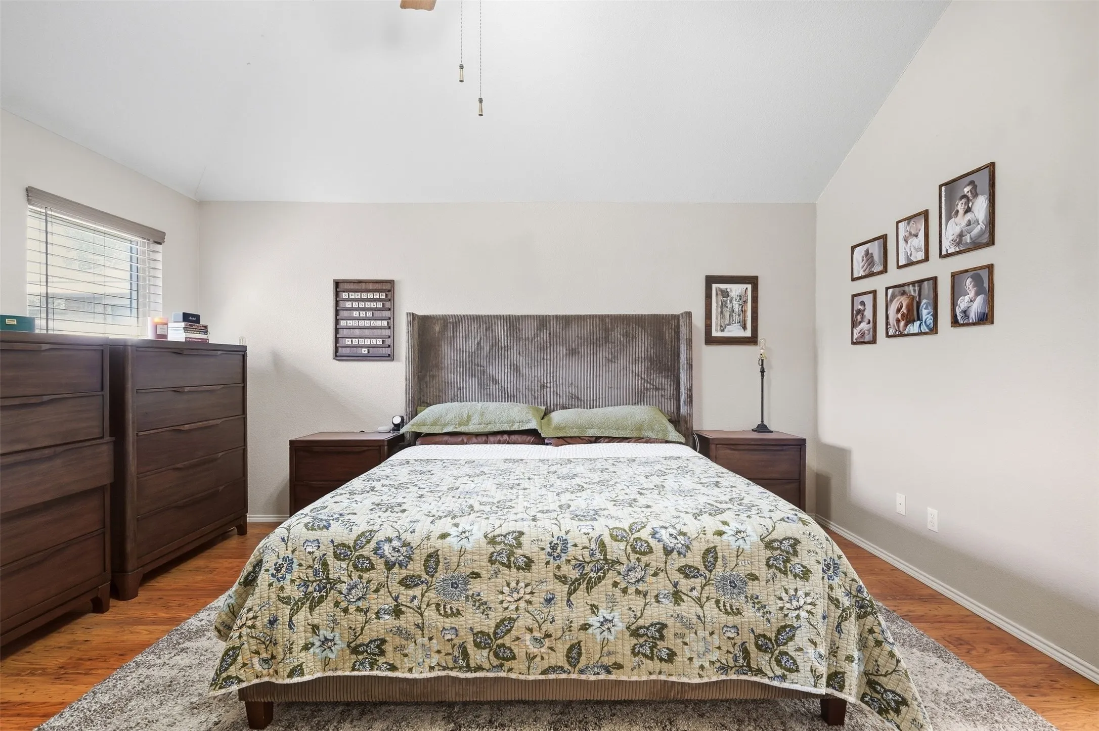 Vaulted ceiling with a ceiling fan, light-toned wall paint, wood-finish flooring, and a window with horizontal blinds
