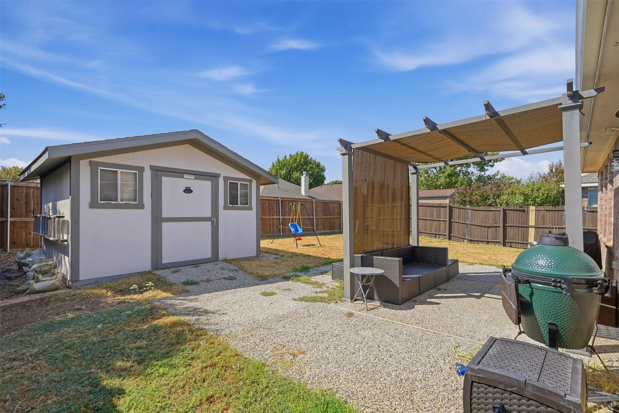 Expansive backyard featuring a gravel patio, covered pergola, and a storage shed