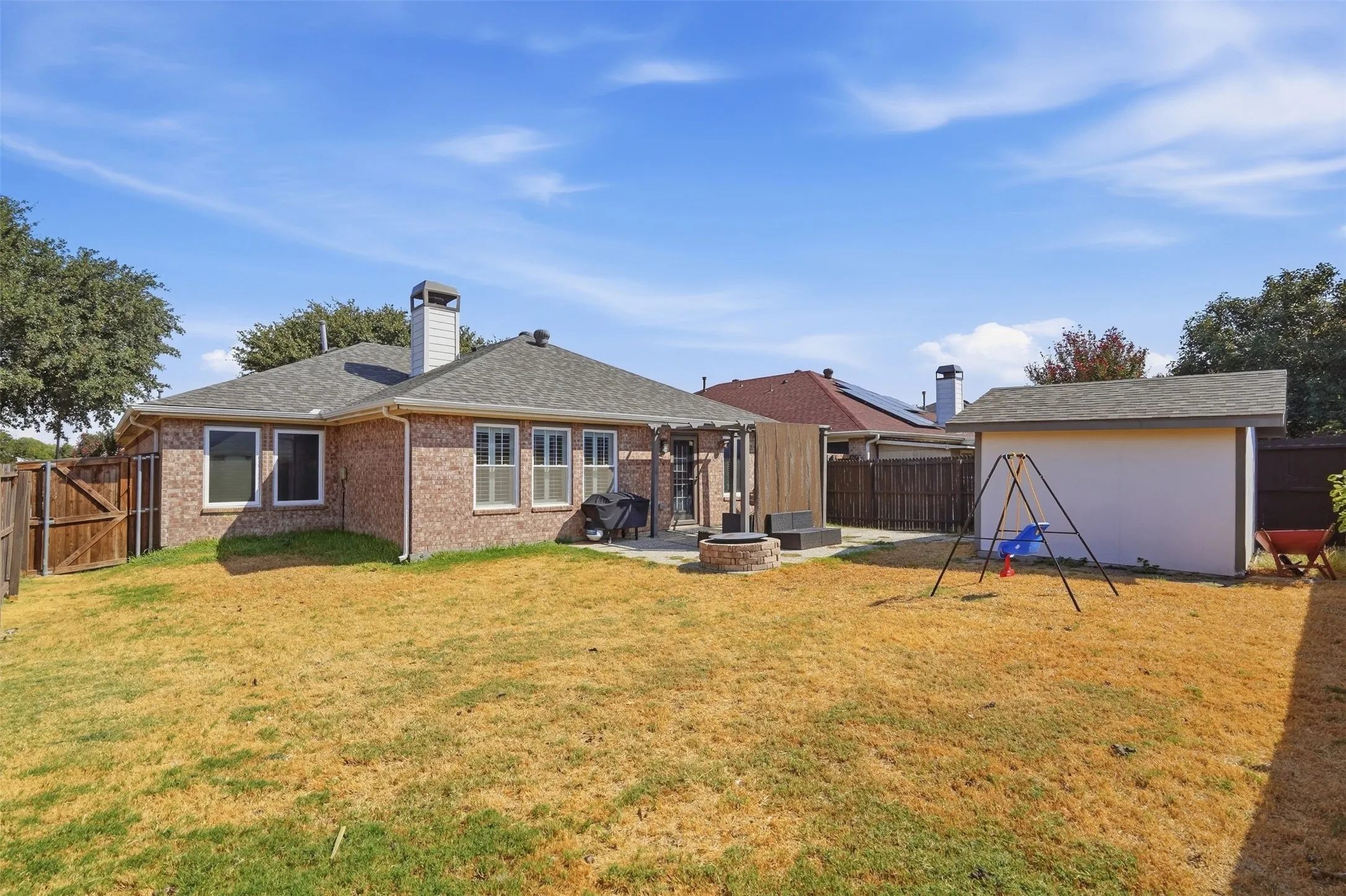 Brick exterior, multiple windows, built-in fire pit, privacy fencing, and a detached shed