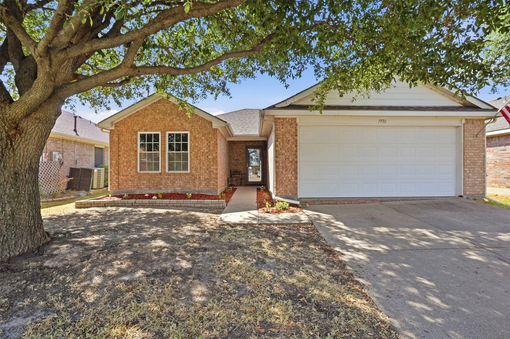 Brick exterior with a white garage door, concrete driveway, and front landscaping