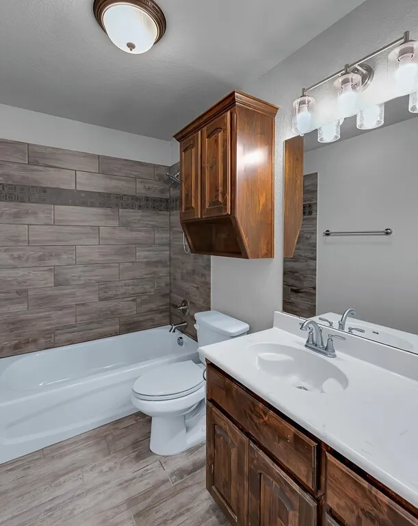 Wood-look tile flooring, wood-finish vanity with an integrated sink, and an overhead lighting fixture