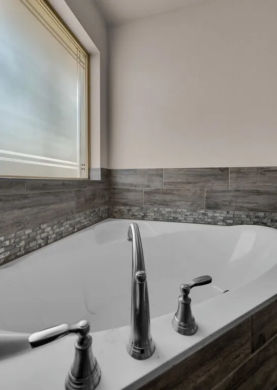 Soaking tub with deck-mounted chrome fixtures, complemented by wood-finish tile wainscoting and a mosaic accent band
